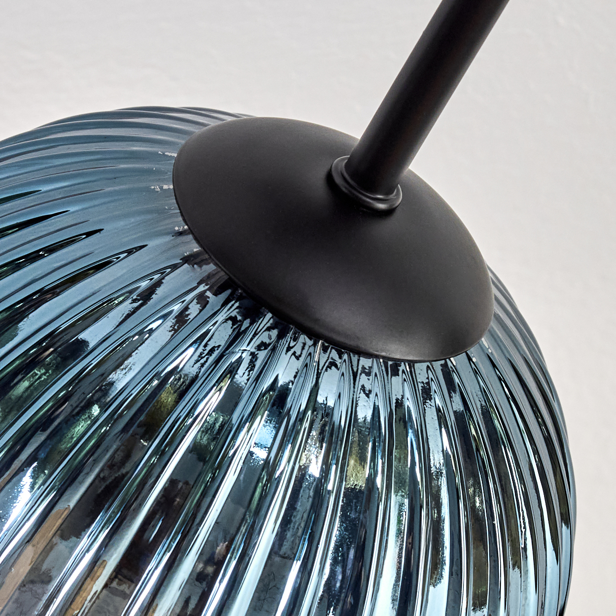 Nahaufnahme eines blauen Glaslampenschirms mit gerippter Textur, gehalten von einer schwarzen Metallstange und -halterung, vor weißem Hintergrund.