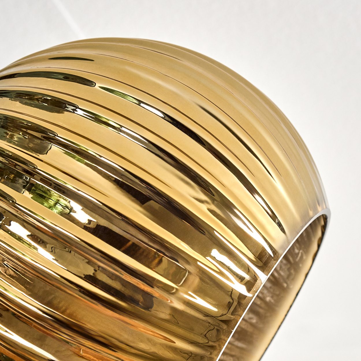 Nahaufnahme einer goldenen, gerippten Leuchte. Das Licht spiegelt sich auf der Oberfläche, mit weißem Hintergrund.