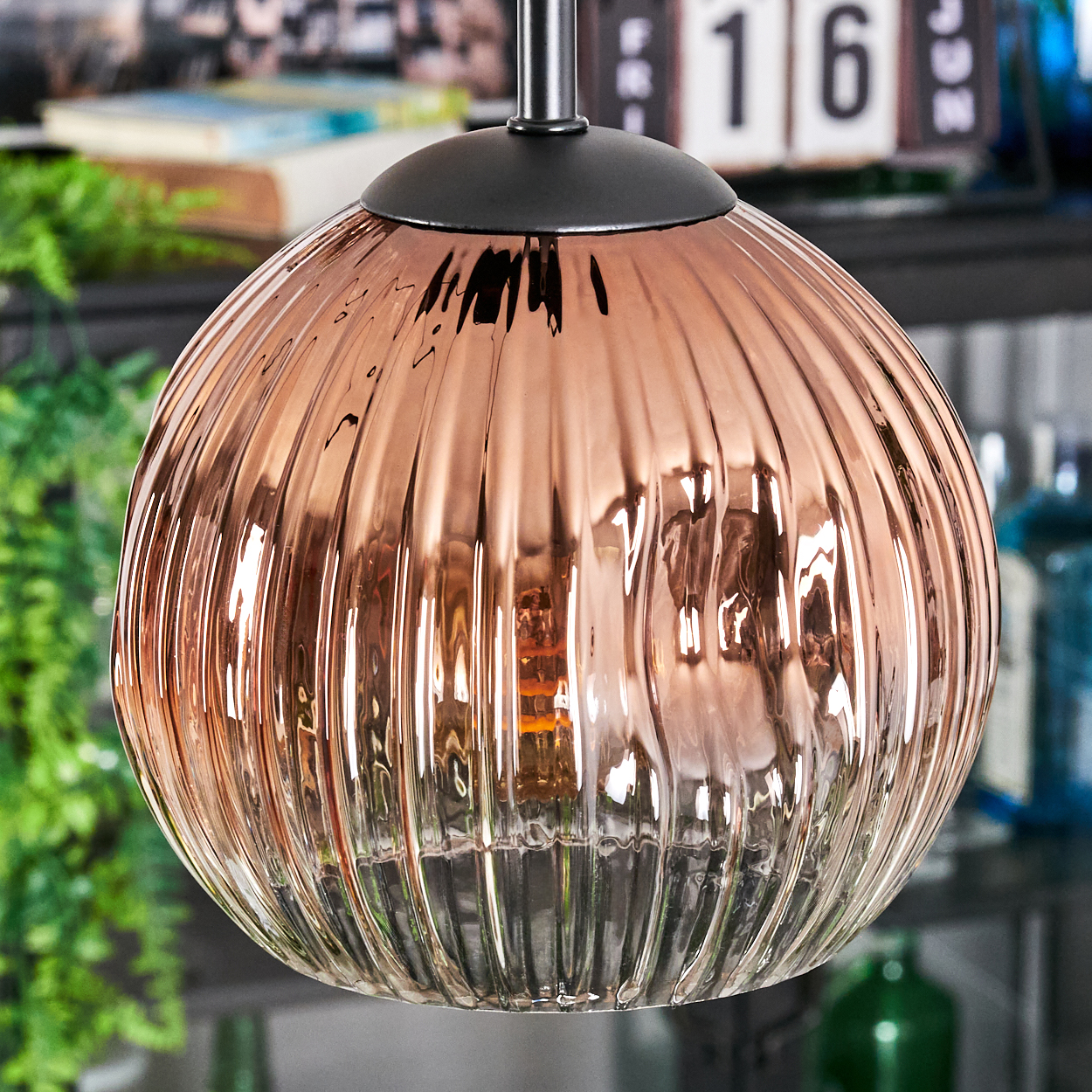 Eine kupferfarbene, geriffelte Glas-Pendelleuchte hängt. Dahinter zeigt ein Kalender '16', und Grün ist sichtbar.