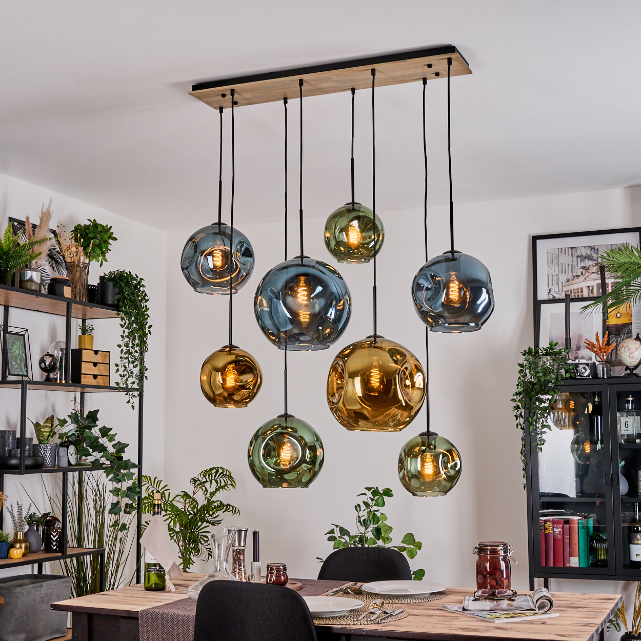 Esszimmer mit Holztisch, hängenden Glaskugelleuchten und Pflanzen. Die Lichter sind in verschiedenen Farben gehalten, Gold, Grün und Blau.