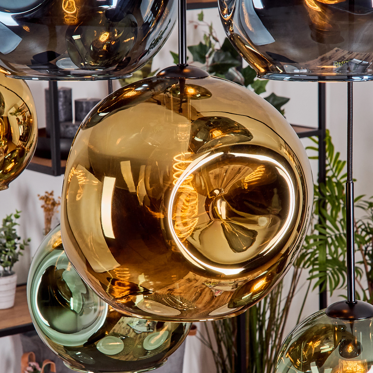 Goldene und grüne Glaskugel-Pendelleuchten. Jede mit einer sichtbaren Wendelglühbirne im Inneren, die an einem schwarzen Kabel hängt.