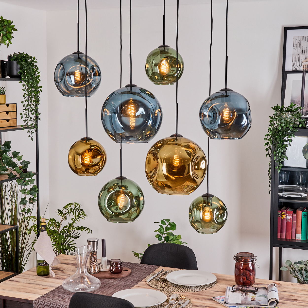 Esszimmer mit mehreren kugelförmigen Pendelleuchten. Ein Holztisch ist mit Tellern und Besteck gedeckt. Pflanzen und Dekoration sind vorhanden.