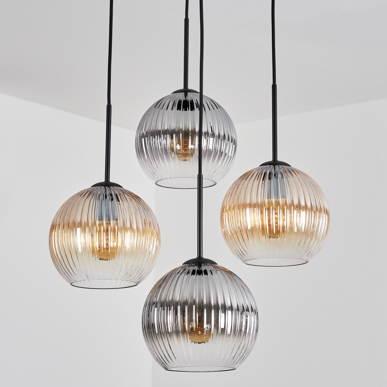 Vier Glaskugel-Pendelleuchten hängen von der Decke. Die Kugeln sind gerippt und haben bernstein- und silberfarbene Töne. Schwarze Kabel.