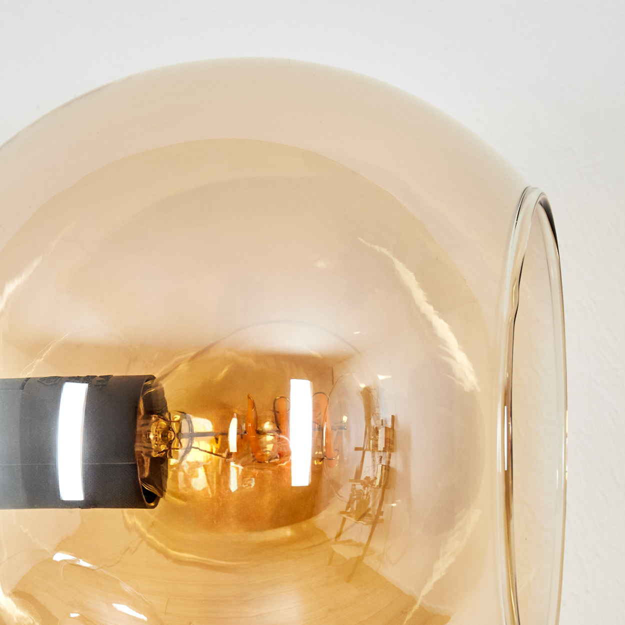 Nahaufnahme einer Glühbirne in einem Glasschirm. Die Glühbirne leuchtet orangefarben. Ein schwarzer Sockel hält die Birne.