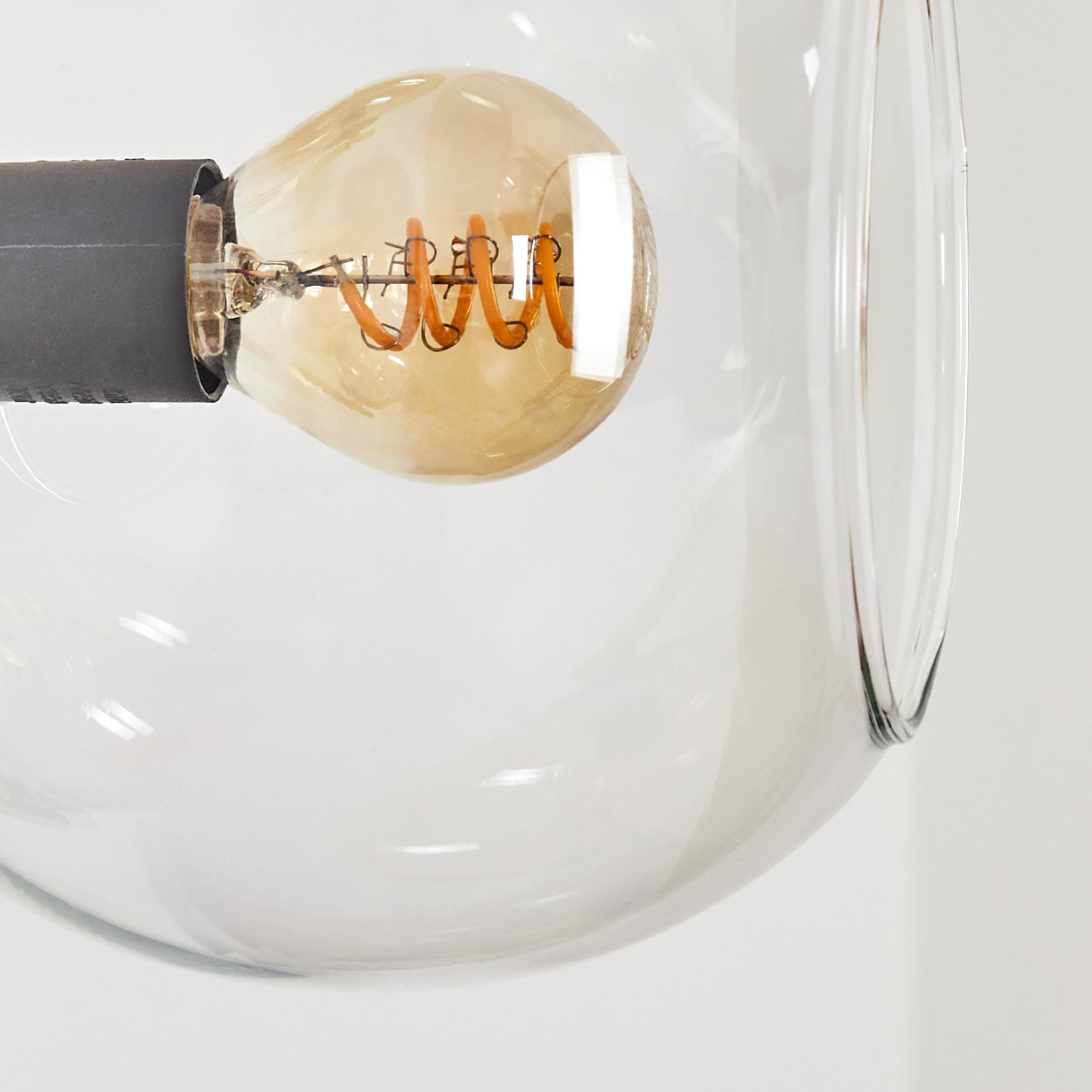 Nahaufnahme einer Glühbirne in einem transparenten Glas. Die Glühbirne ist orangefarben und hat einen Spiralfaden. Das Glas ist rund.