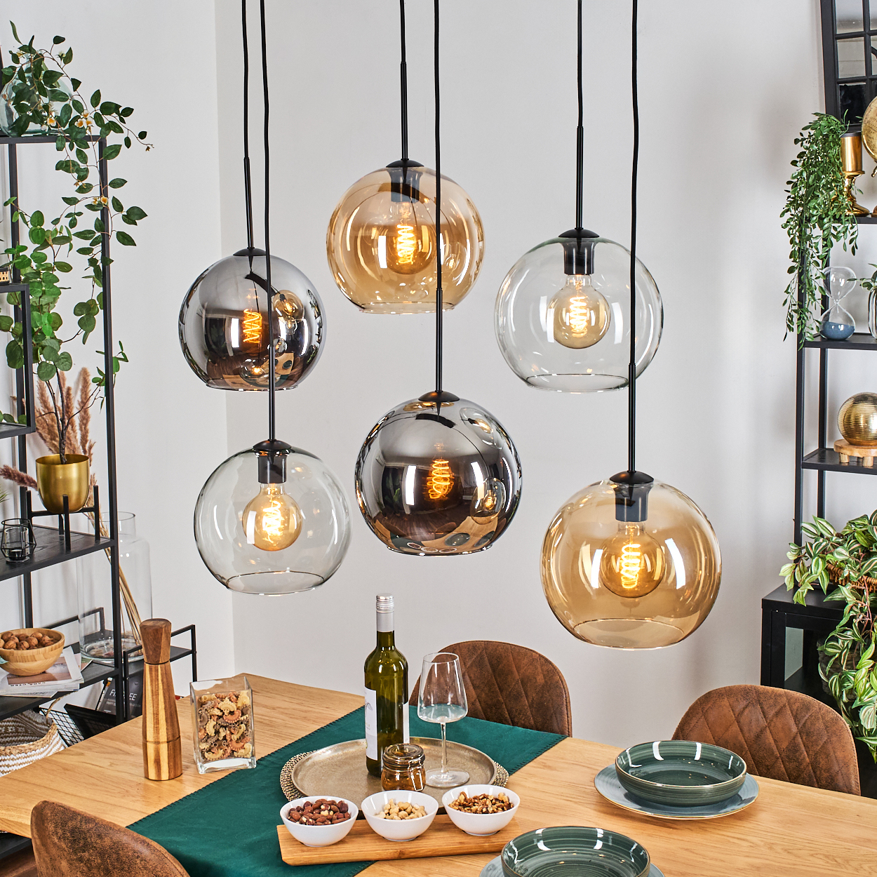 Esszimmer mit sechs hängenden Kugelleuchten. Tisch mit Snacks, Tellern und Wein. Regale mit Pflanzen im Hintergrund.