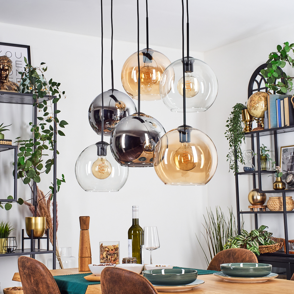 Esszimmer mit Holztisch, hängenden Kugelleuchten und Dekoration auf Regalen. Teller, Wein und Stühle sind sichtbar.