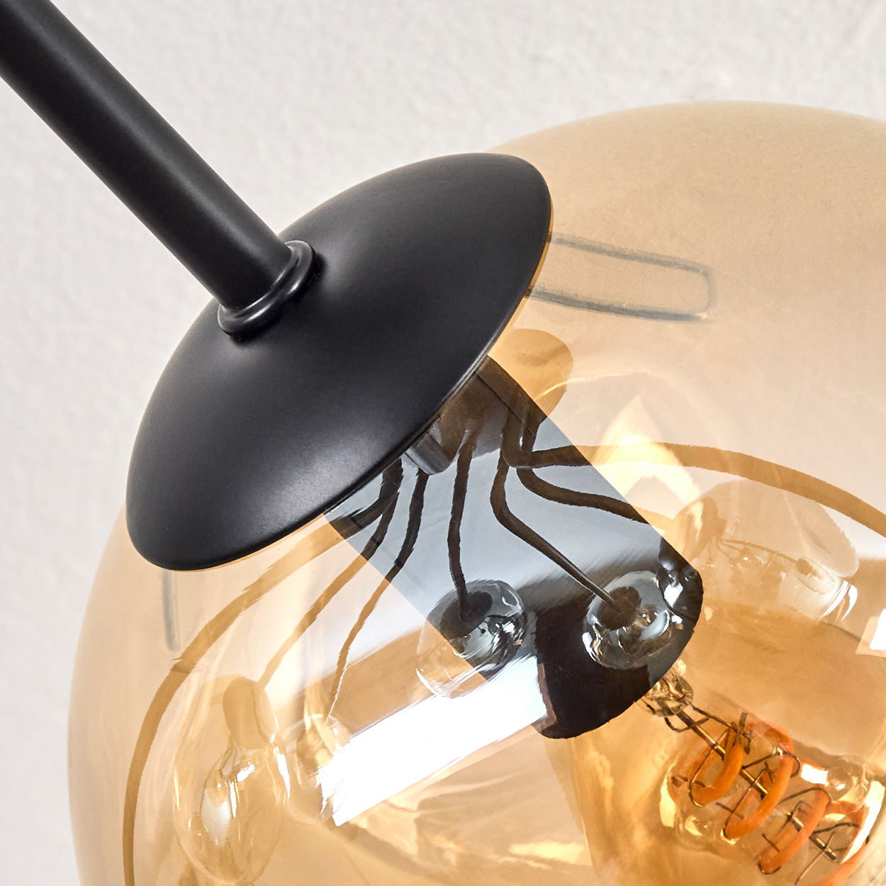 Nahaufnahme einer modernen Lampe mit schwarzem Stiel und transparentem, bernsteinfarbenem Glasschirm, zeigt die Glühbirne.