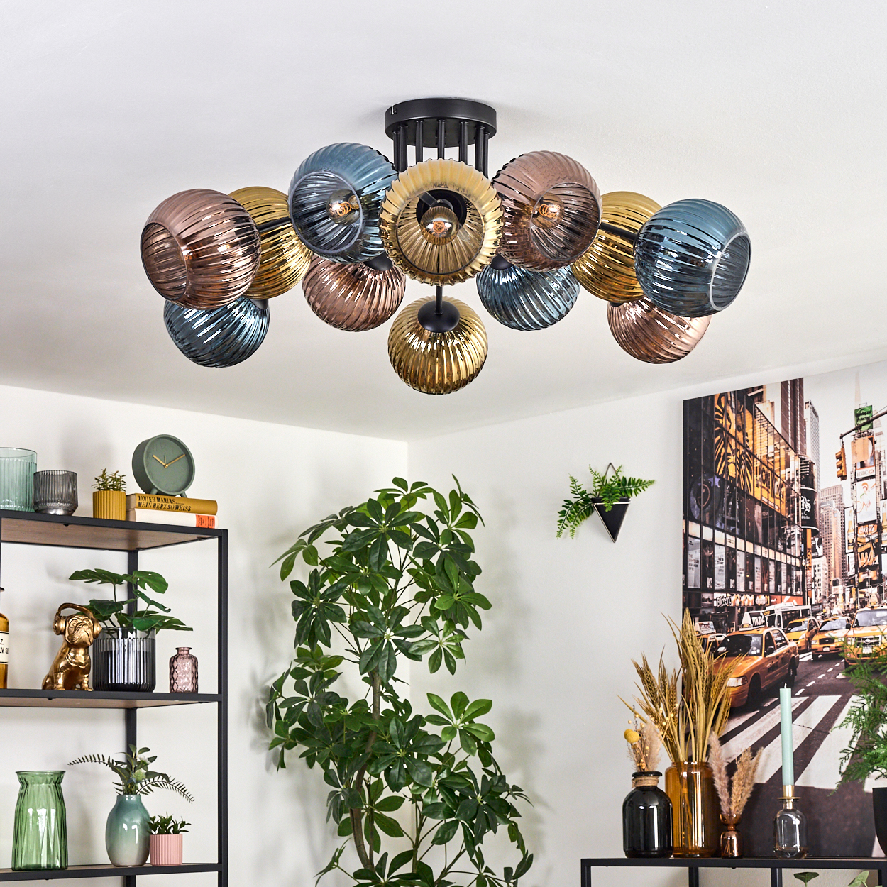 Eine moderne Deckenleuchte mit verschiedenfarbigen Glaskugeln hängt von der Decke. Pflanzen, Regale mit Dekor und ein Stadtbild-Kunstwerk.
