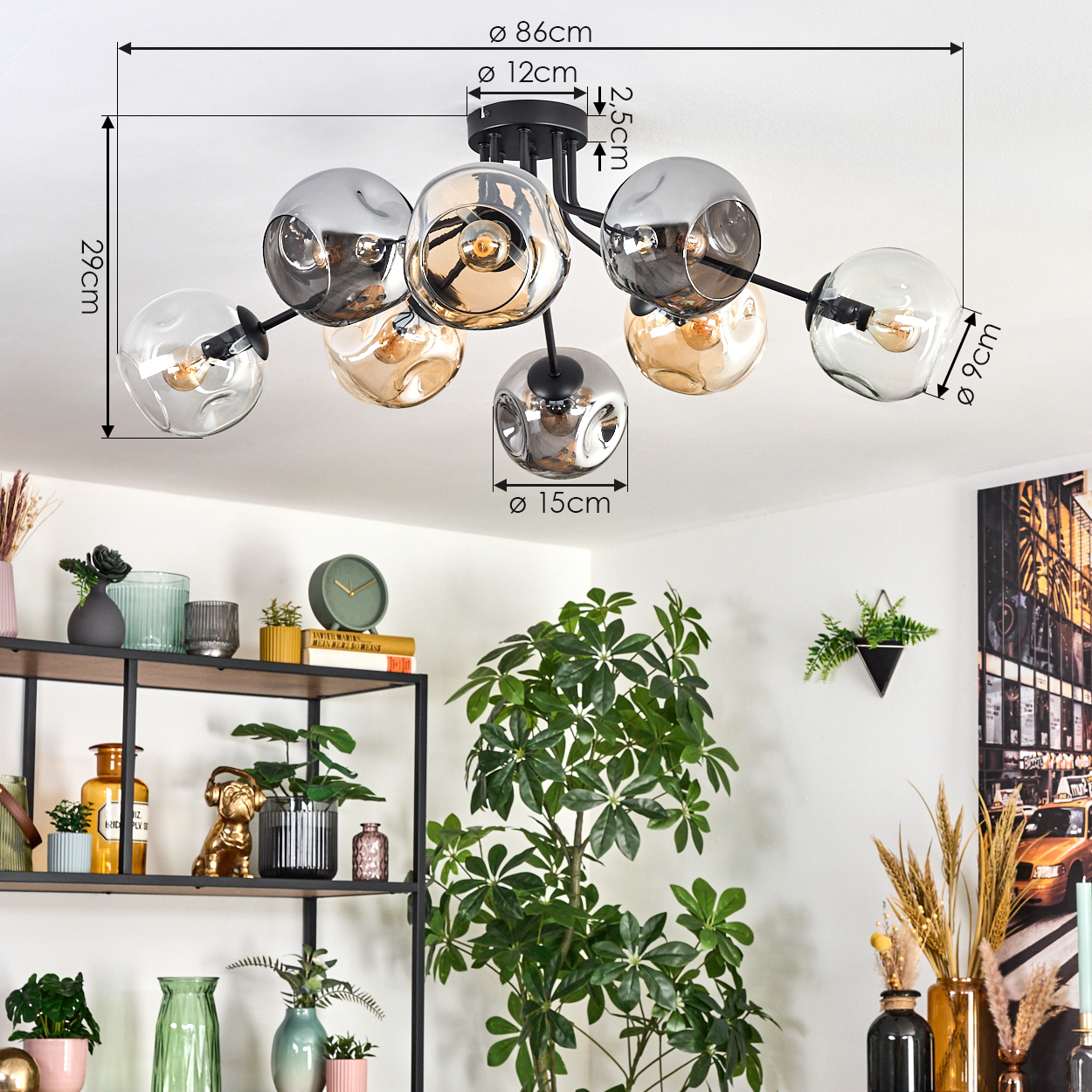 Eine moderne Deckenlampe mit Glaskugeln und schwarzem Rahmen hängt. Ein Regal mit Dekor und eine große grüne Pflanze darunter.