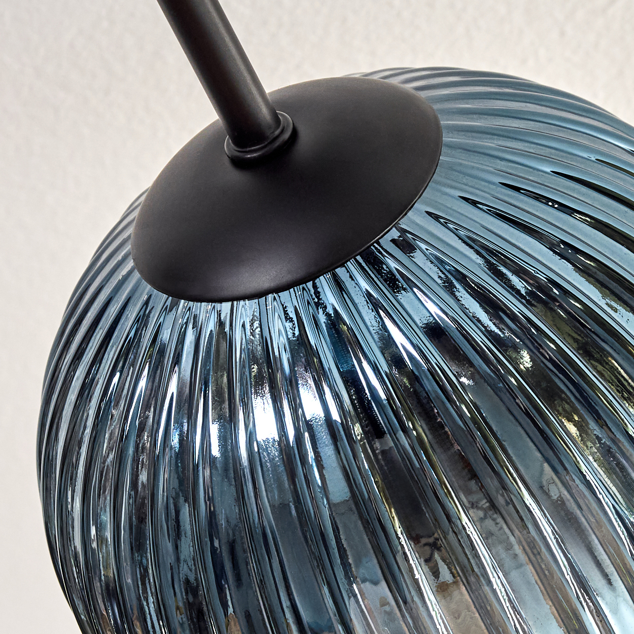 Nahaufnahme einer Glasleuchte. Das blaue, gerippte Glas befindet sich unter einer schwarzen Metallkappe und einem Stab.