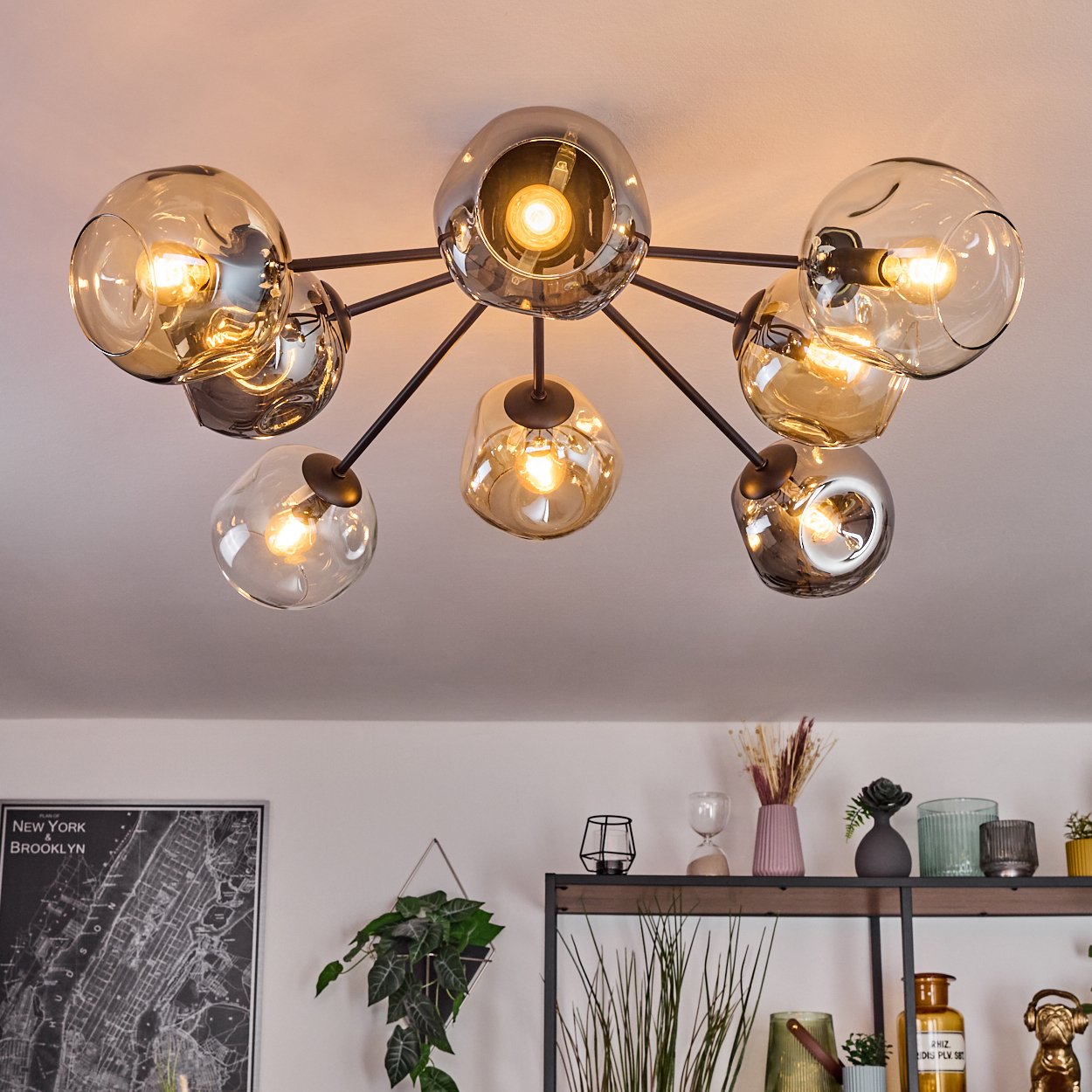 Eine moderne Deckenleuchte mit Glaskugeln und Edison-Glühbirnen. Im Hintergrund ein Regal mit Dekor und eine New York-Karte.