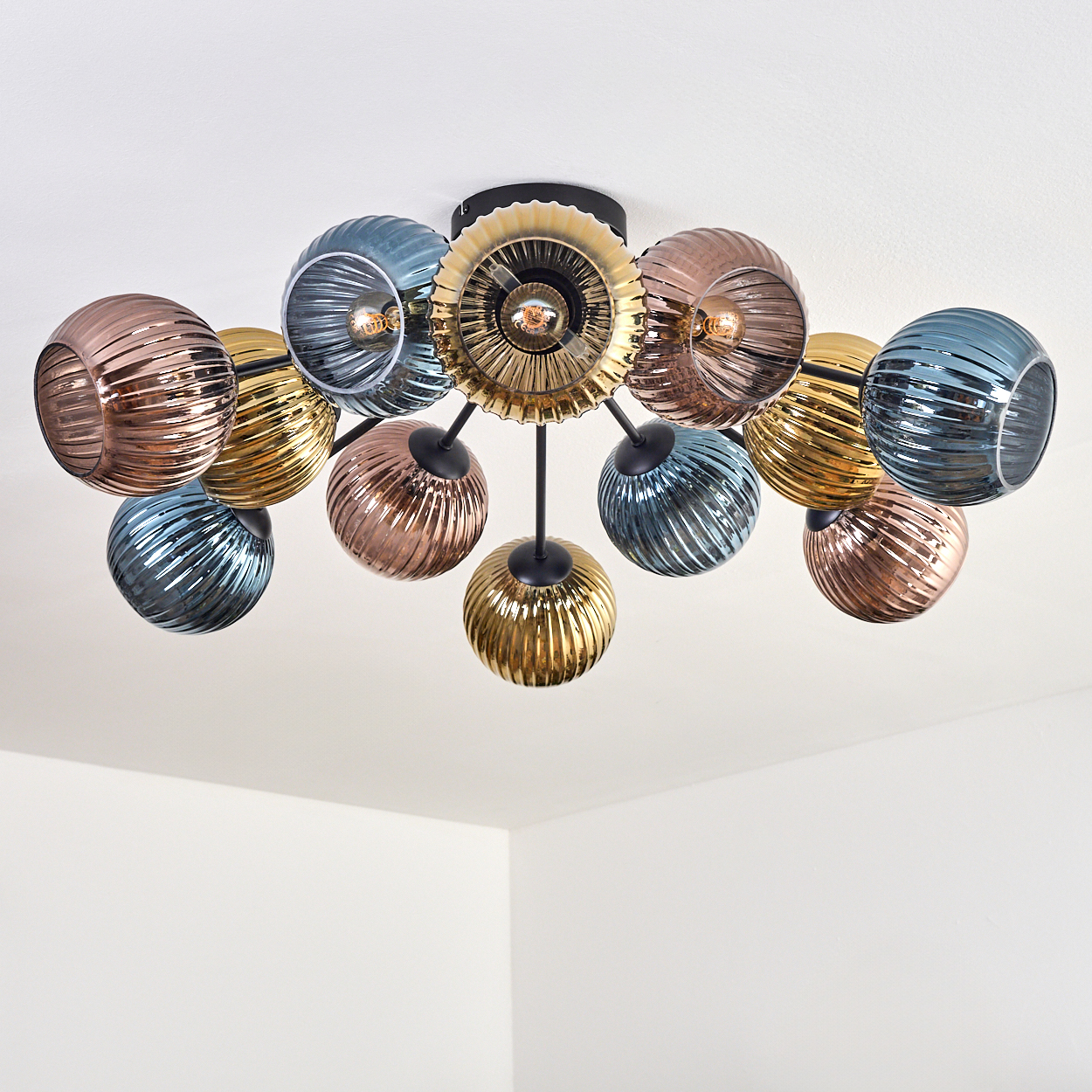 Eine moderne Deckenleuchte mit farbigen Glaskugeln. Farben sind Blau, Gold und Kupfer. Der Hintergrund ist eine weiße Decke.