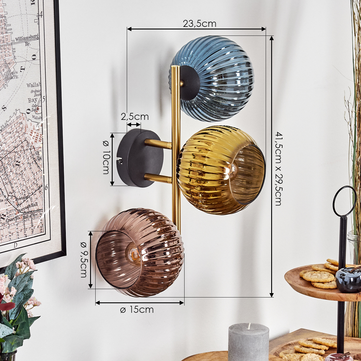 Eine Wandlampe mit drei Glaskugeln in Blau, Gold und Rosa, getragen von einem Messingstiel, an einer weißen Wand befestigt. Abmessungen sind enthalten.