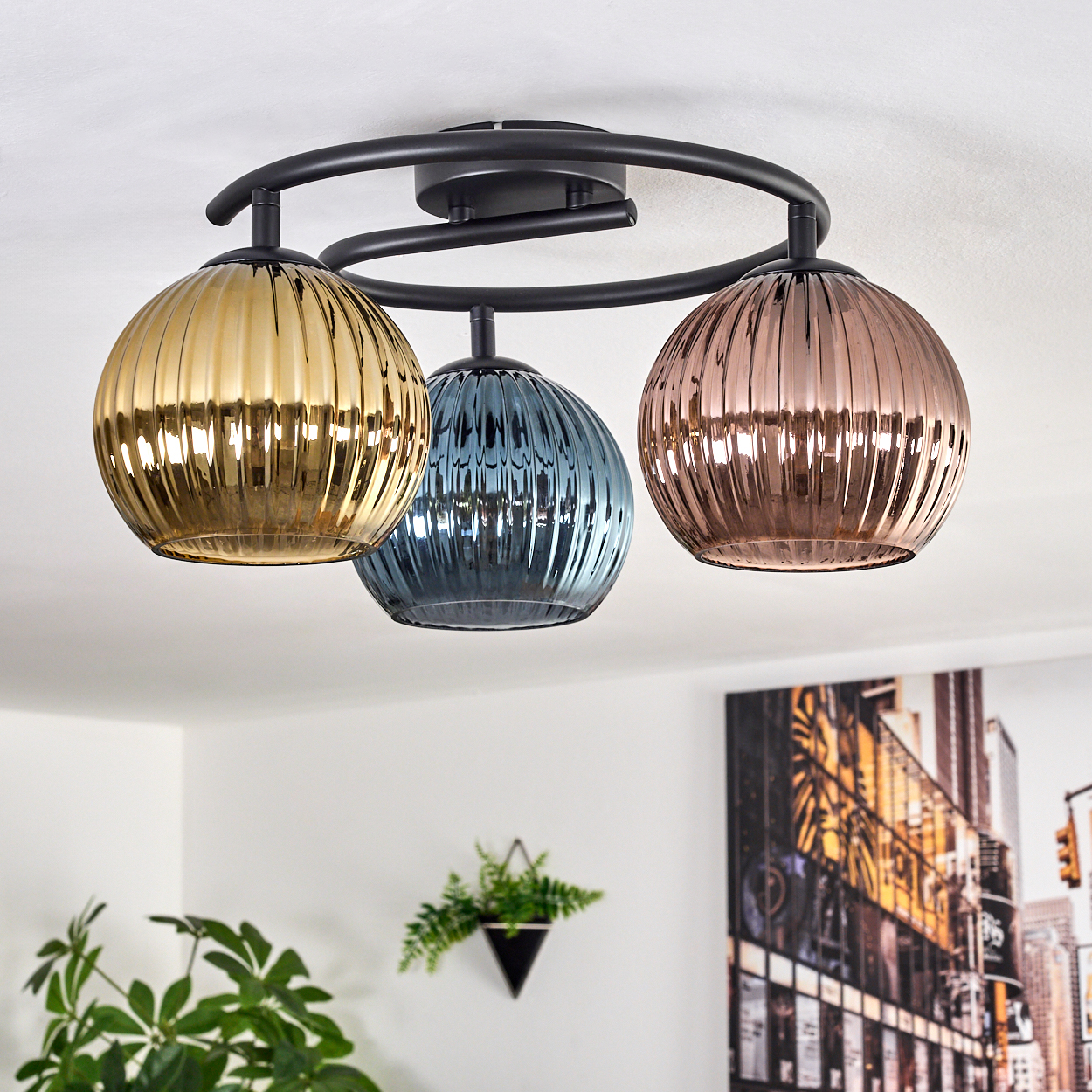 Deckenleuchte mit drei Glaskugeln in Gold, Blau und Kupfer. Die Halterung ist schwarz, die Decke weiß.