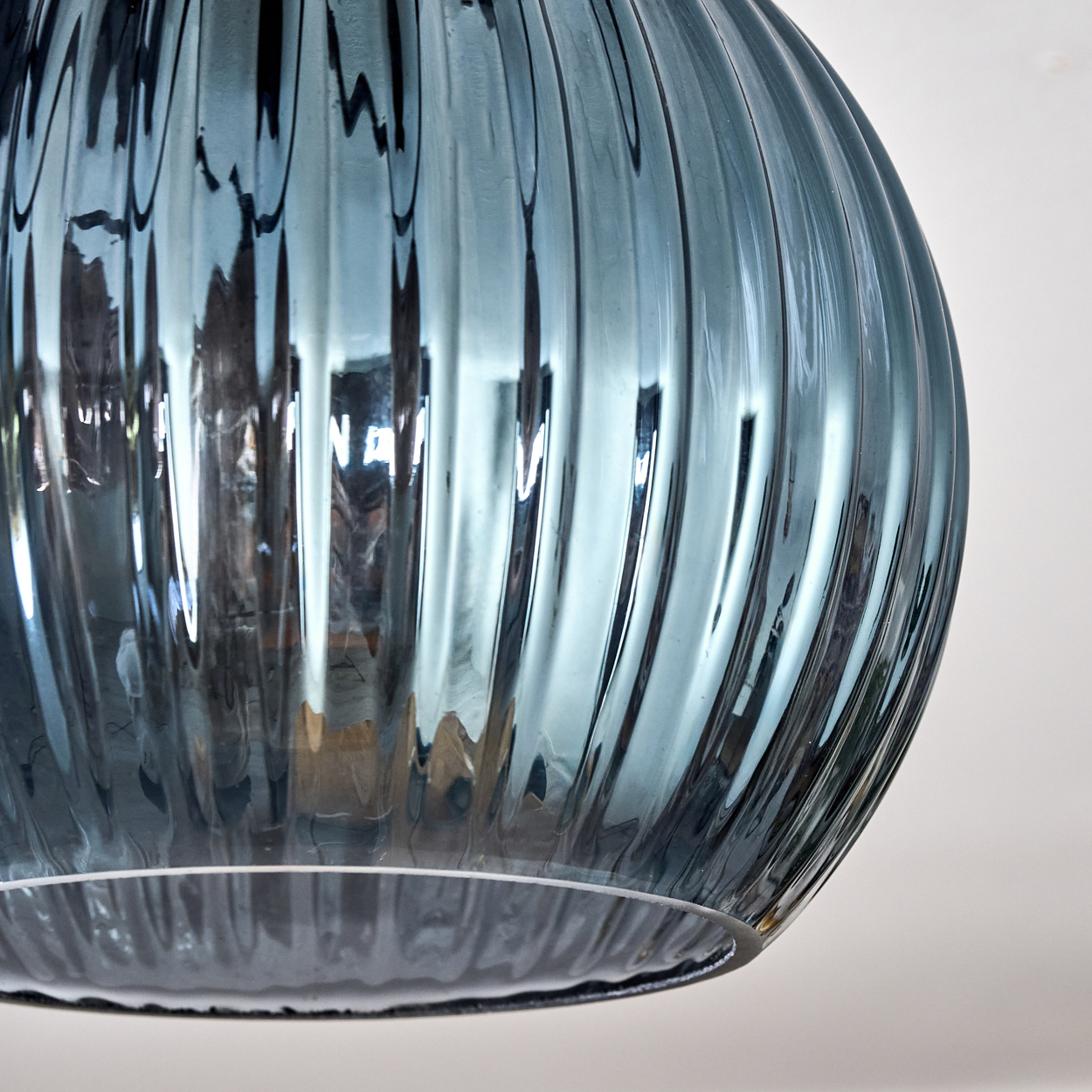 Nahaufnahme eines blauen Glasobjekts mit vertikalen Rippen. Das Glas reflektiert Licht, der Hintergrund ist weiß.