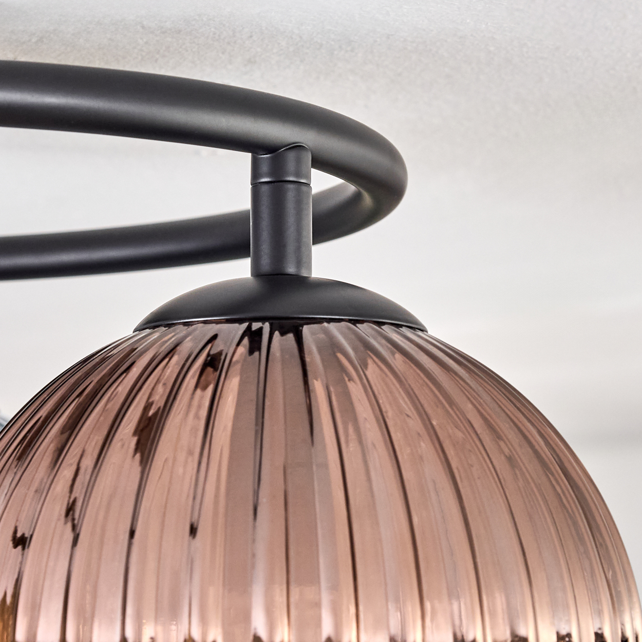 Nahaufnahme einer modernen Leuchte. Sie hat einen bronzefarbenen Glasschirm mit vertikalen Rippen und einen schwarzen Metallrahmen.