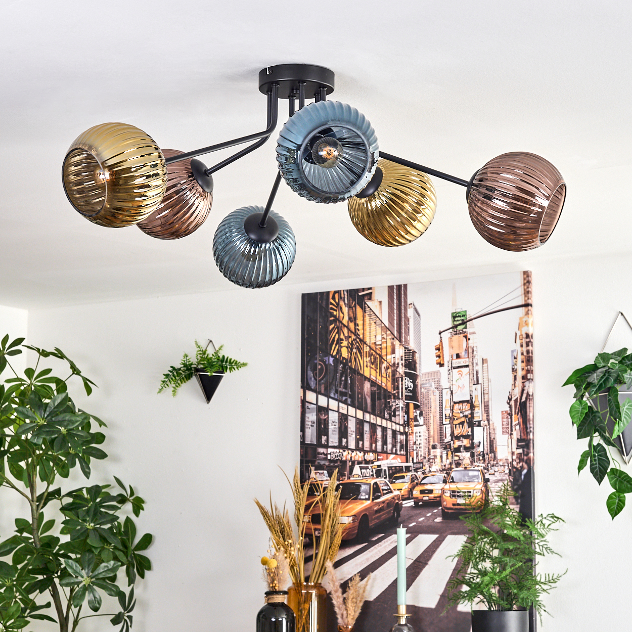 Eine moderne Deckenlampe mit sechs bunten Glaskugeln. Im Hintergrund ein Stadtbild und Pflanzen.