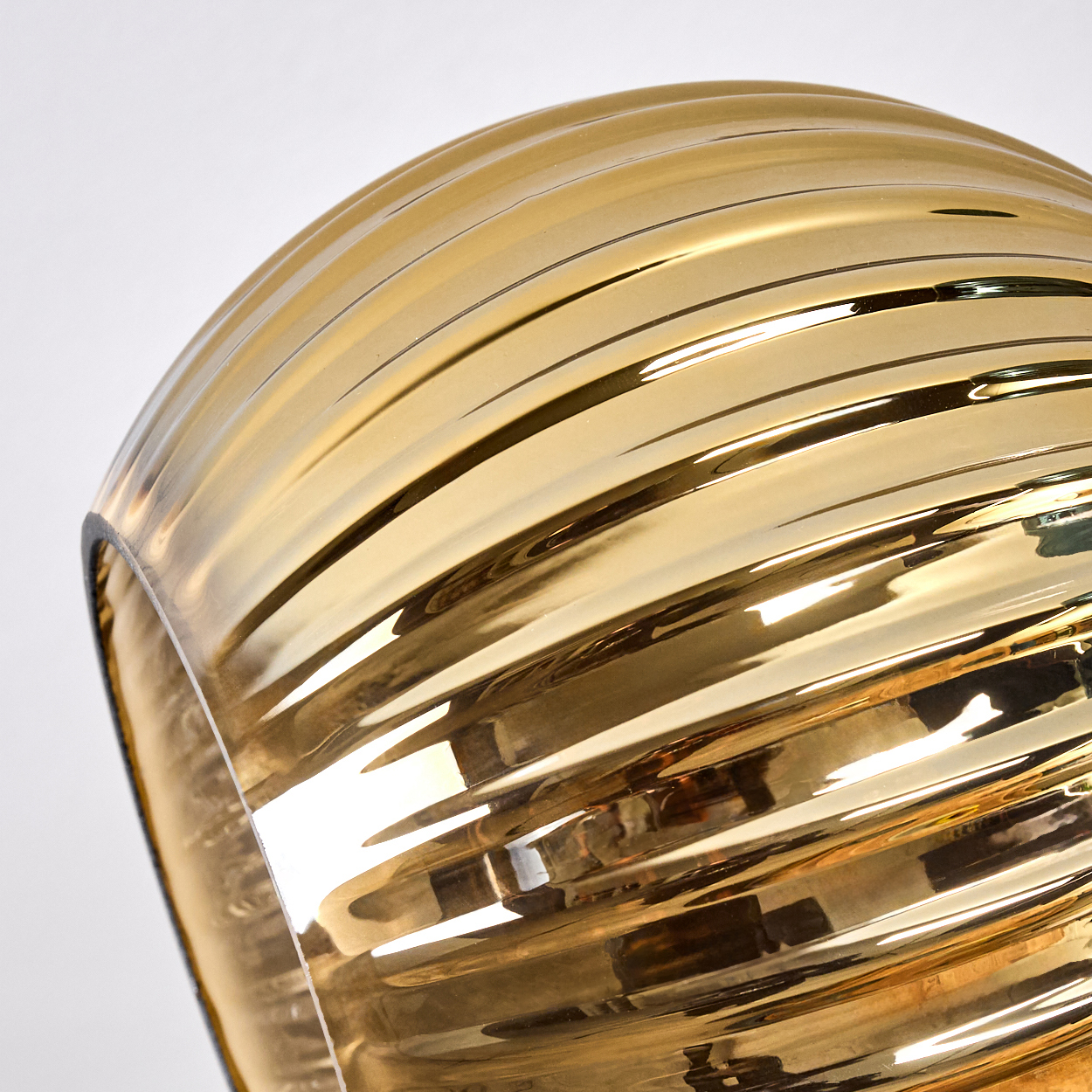 Nahaufnahme eines goldenen Glaslampenschirms mit horizontalen Rippen. Der Hintergrund ist weiß.