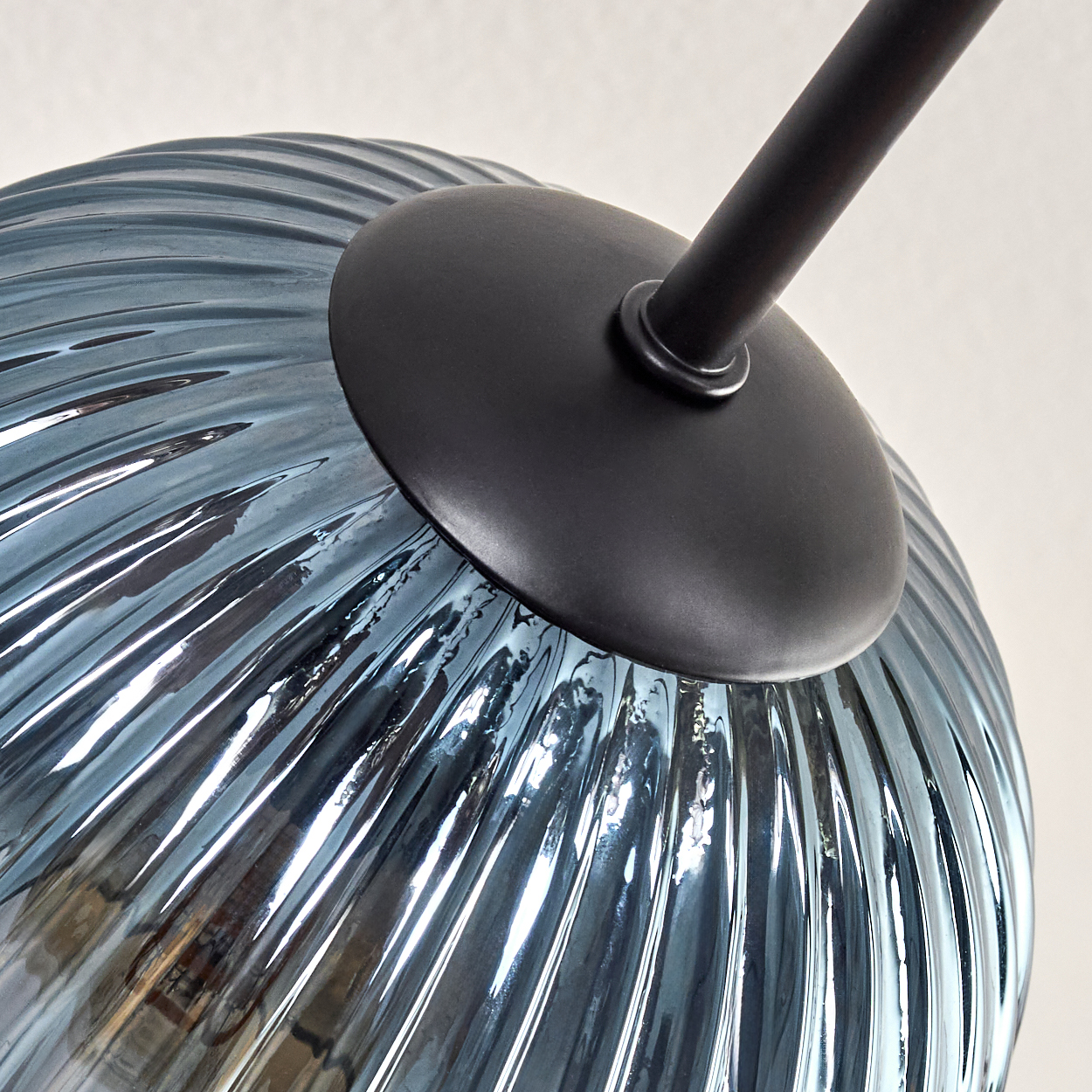 Nahaufnahme eines blauen Glaslampenschirms mit gerippter Textur. Ein schwarzer Metallarm und eine kreisförmige Basis sind angebracht.