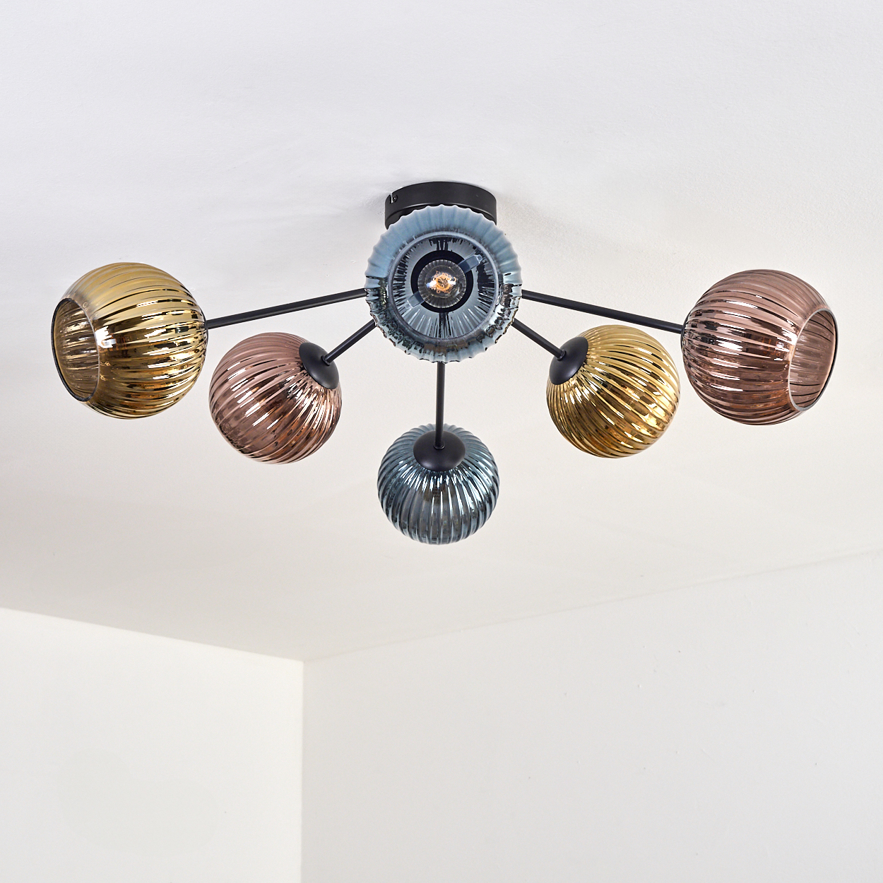 Eine moderne Deckenleuchte mit sechs Glasschirmen in verschiedenen Farben: Gold, Kupfer und Türkis, montiert auf einem schwarzen Rahmen.