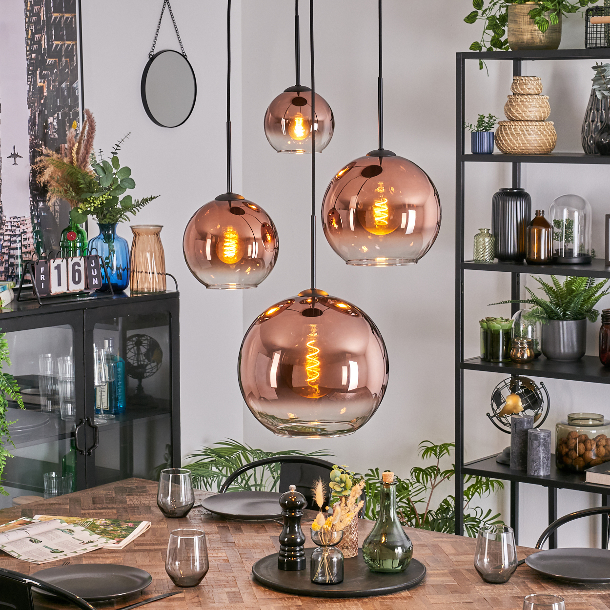 Esszimmer mit kupferfarbenen Pendelleuchten. Holztisch mit Tellern und Gläsern. Regale mit Deko im Hintergrund.