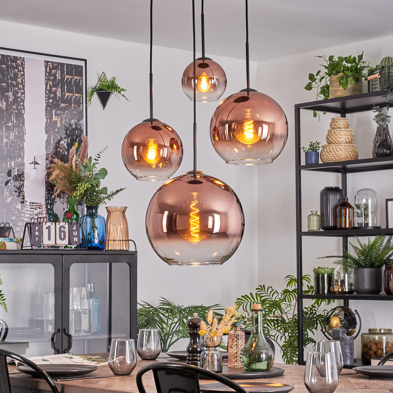 Esszimmer mit kupferfarbenen Pendelleuchten. Tisch mit Gläsern und Tellern. Regale mit Pflanzen und Dekoration.