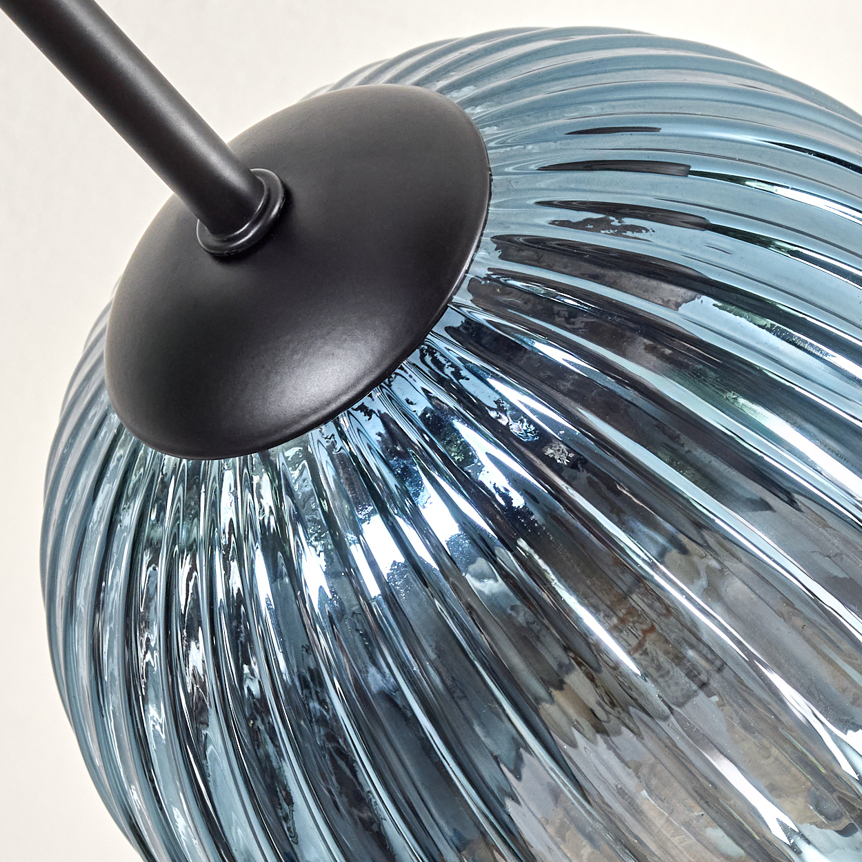 Nahaufnahme eines blauen Glaslampenschirms mit Spiralmuster. Ein schwarzer Metallarm und -anschluss befinden sich oben.
