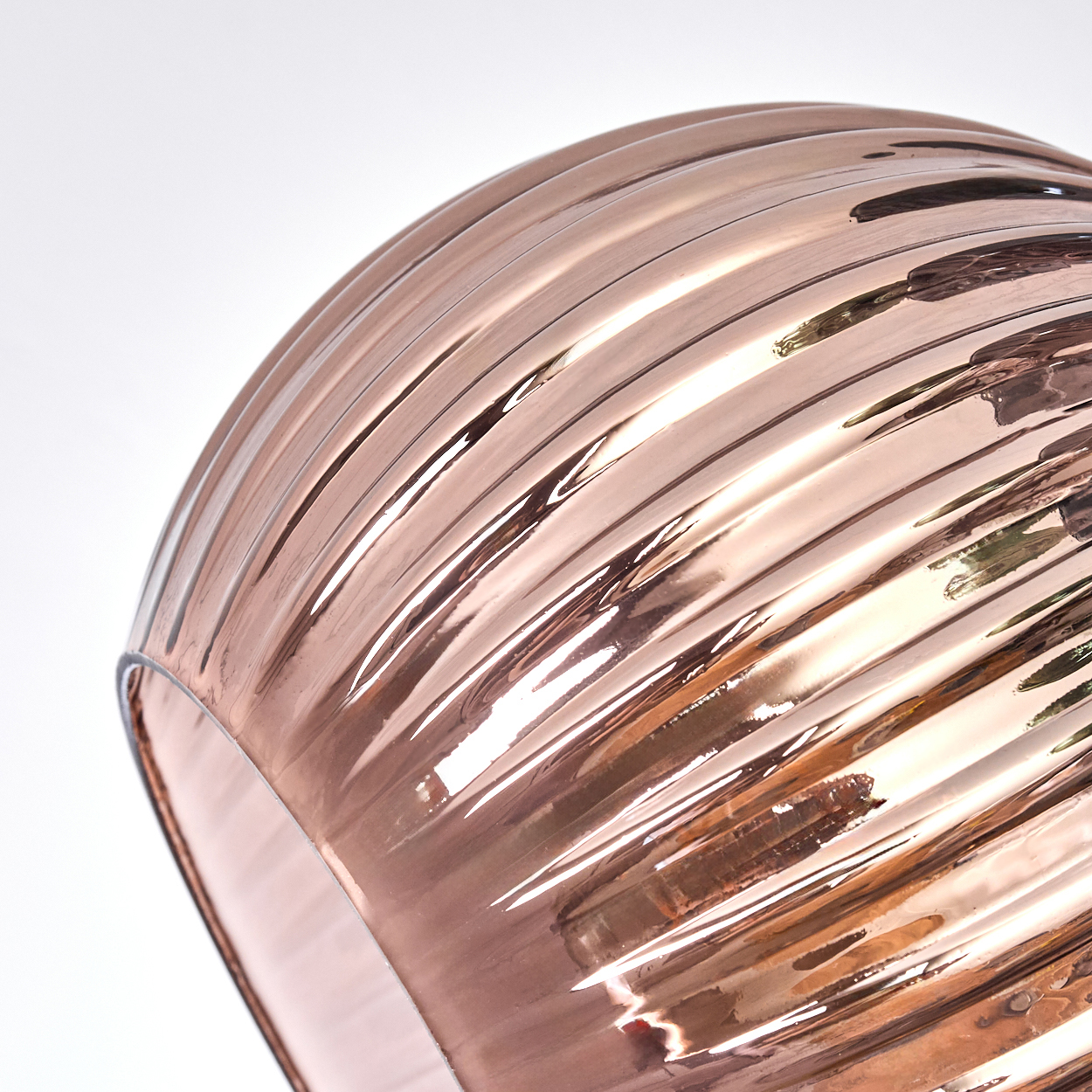 Nahaufnahme eines roségoldenen, gerippten Glasobjekts. Das Licht reflektiert von der gewölbten Oberfläche. Der Hintergrund ist weiß.