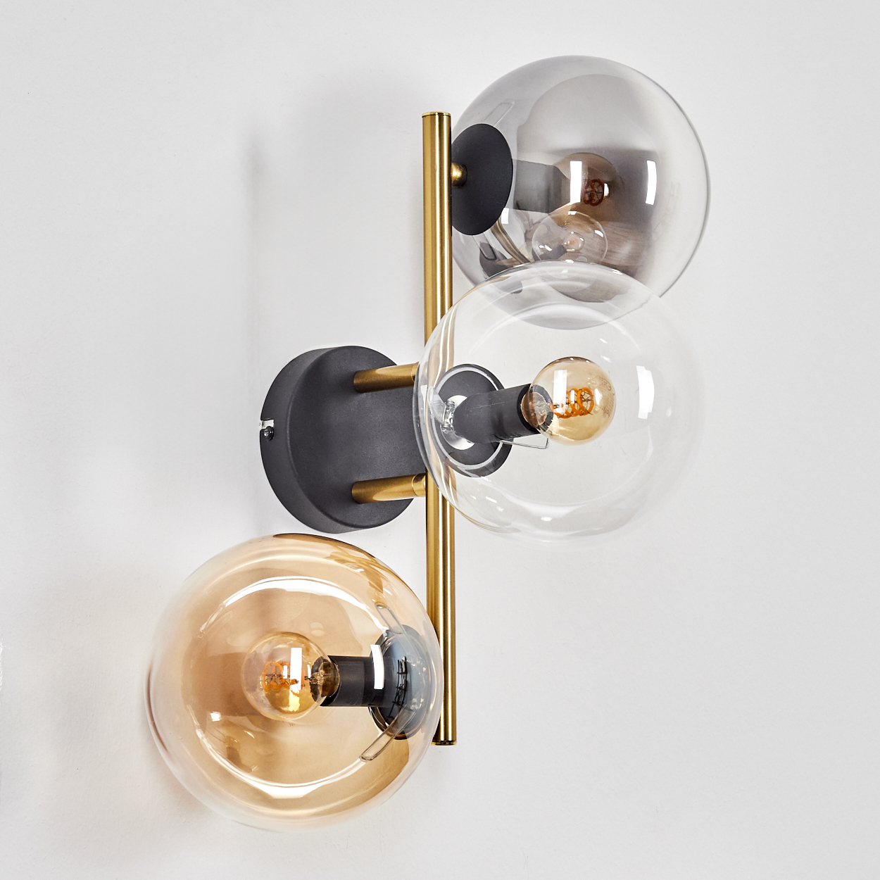 Eine moderne Wandlampe mit drei Glaskugeln. Die obere ist grau getönt, die mittlere klar und die untere bernsteinfarben.