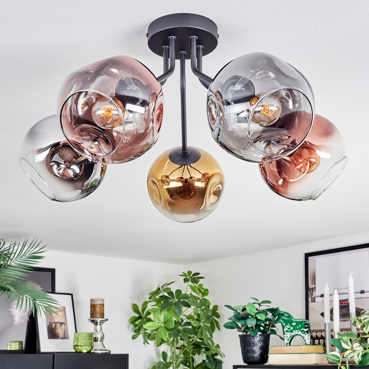 Eine moderne Deckenleuchte mit fünf Glaskugel-Schirmen in Rosé-, Gold- und Silbertönen. Pflanzen und Dekorationen sind unten.
