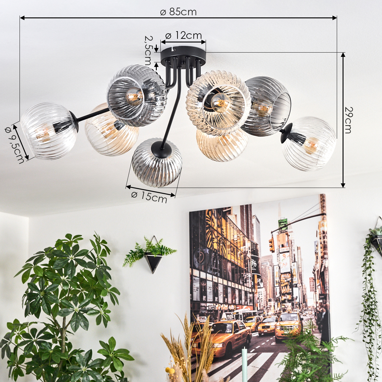 Eine moderne Deckenlampe mit Glaskugeln, Maße beschriftet. Ein Stadtbild-Kunstwerk an der Wand hinter Pflanzen.