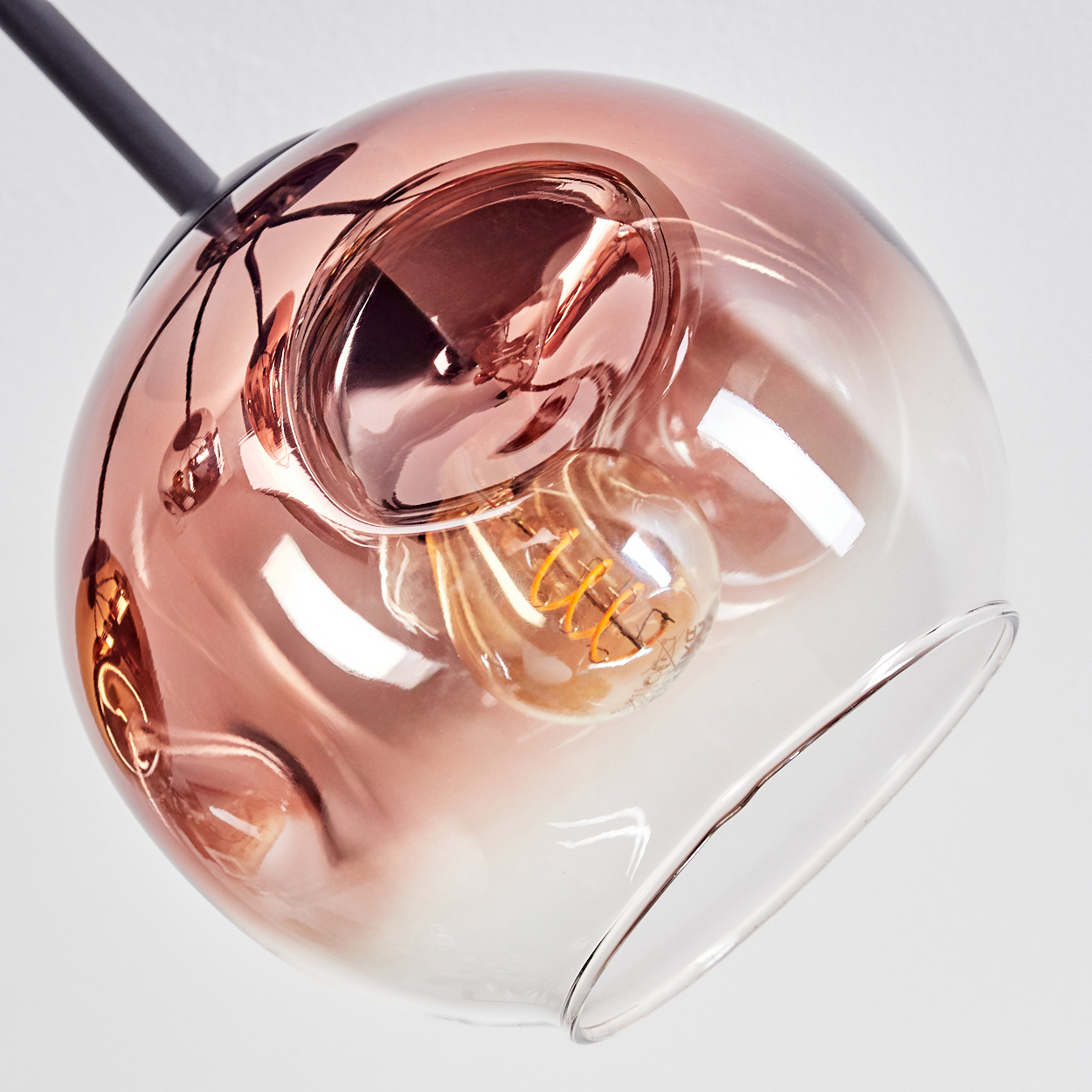 Eine moderne Glas-Pendelleuchte mit kupferfarbenem Schirm, sichtbarer Glühbirne und schwarzem Stiel, vor weißem Hintergrund.