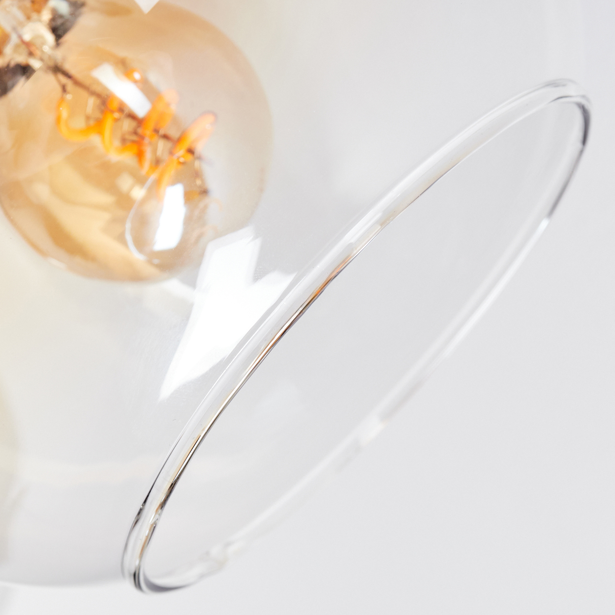 Nahaufnahme einer Glaslampe mit sichtbarer Glühbirne. Die Lampe hat einen klaren, gebogenen Glasschirm. Der Hintergrund ist weiß.