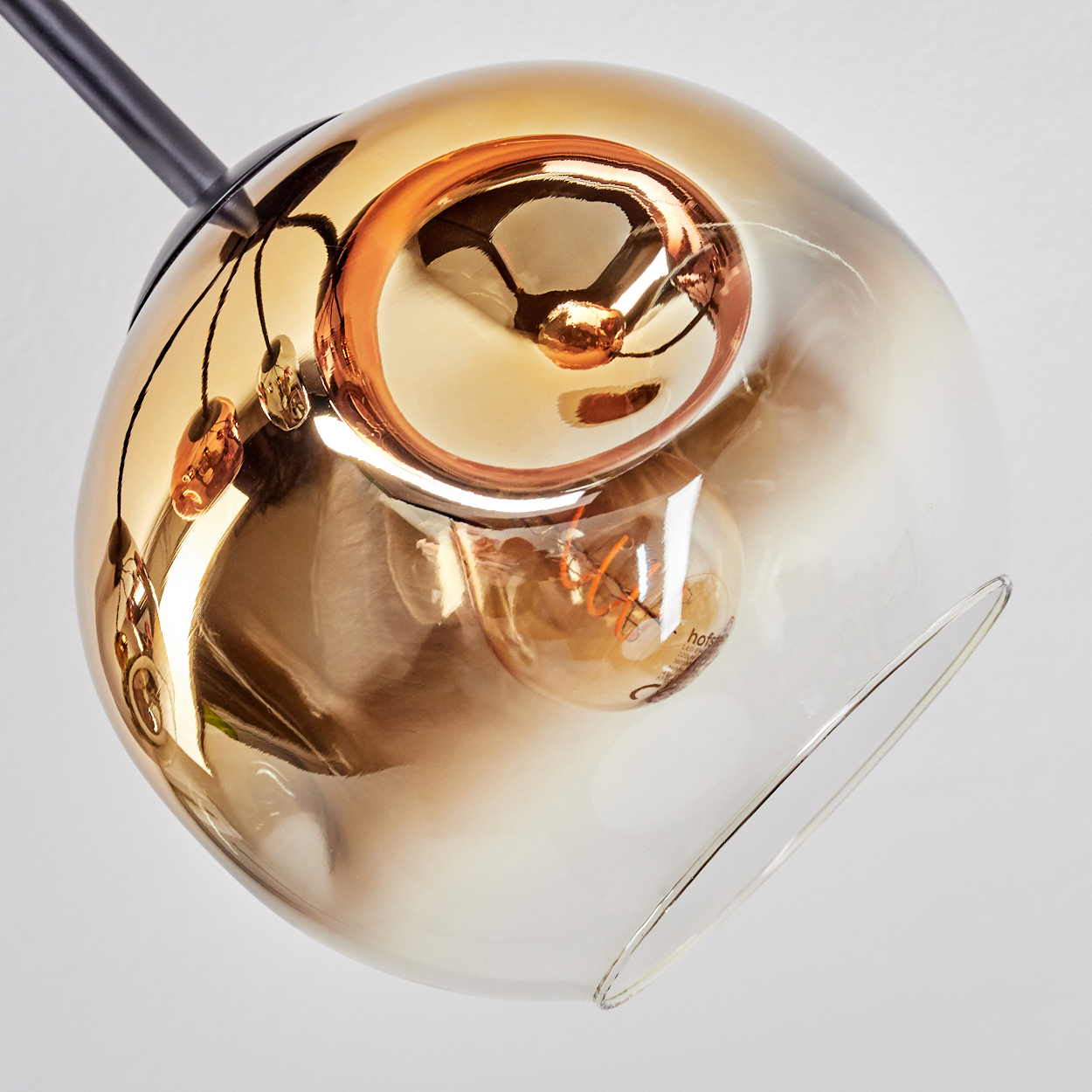 Eine moderne, kugelförmige Glaslampe hängt vor einem weißen Hintergrund. Das Glas ist bernsteinfarben, mit einer Glühbirne im Inneren.