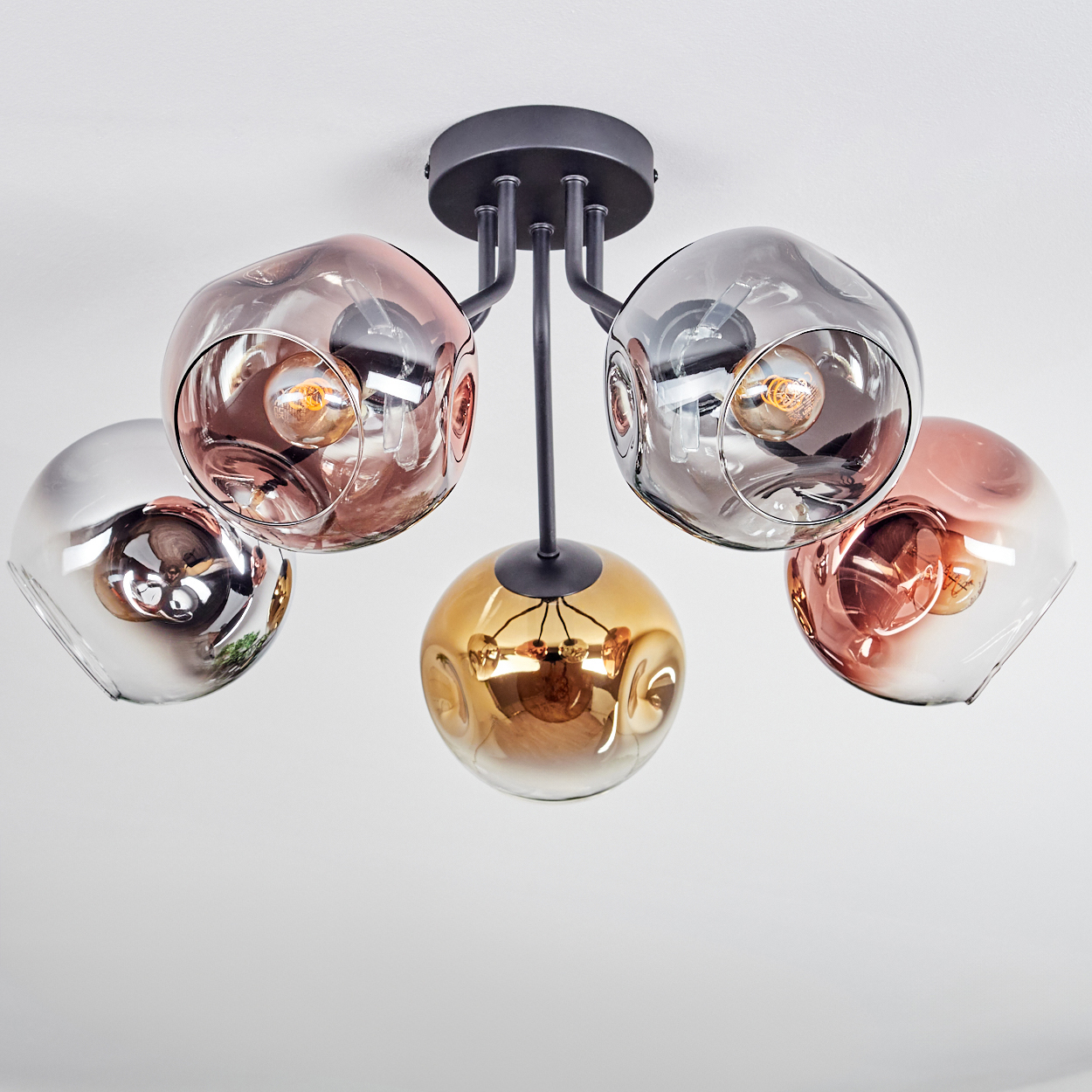 Eine moderne Deckenleuchte mit fünf Glasschirmen in Silber, Gold und Rosé. Die Leuchte ist an einer weißen Decke montiert.