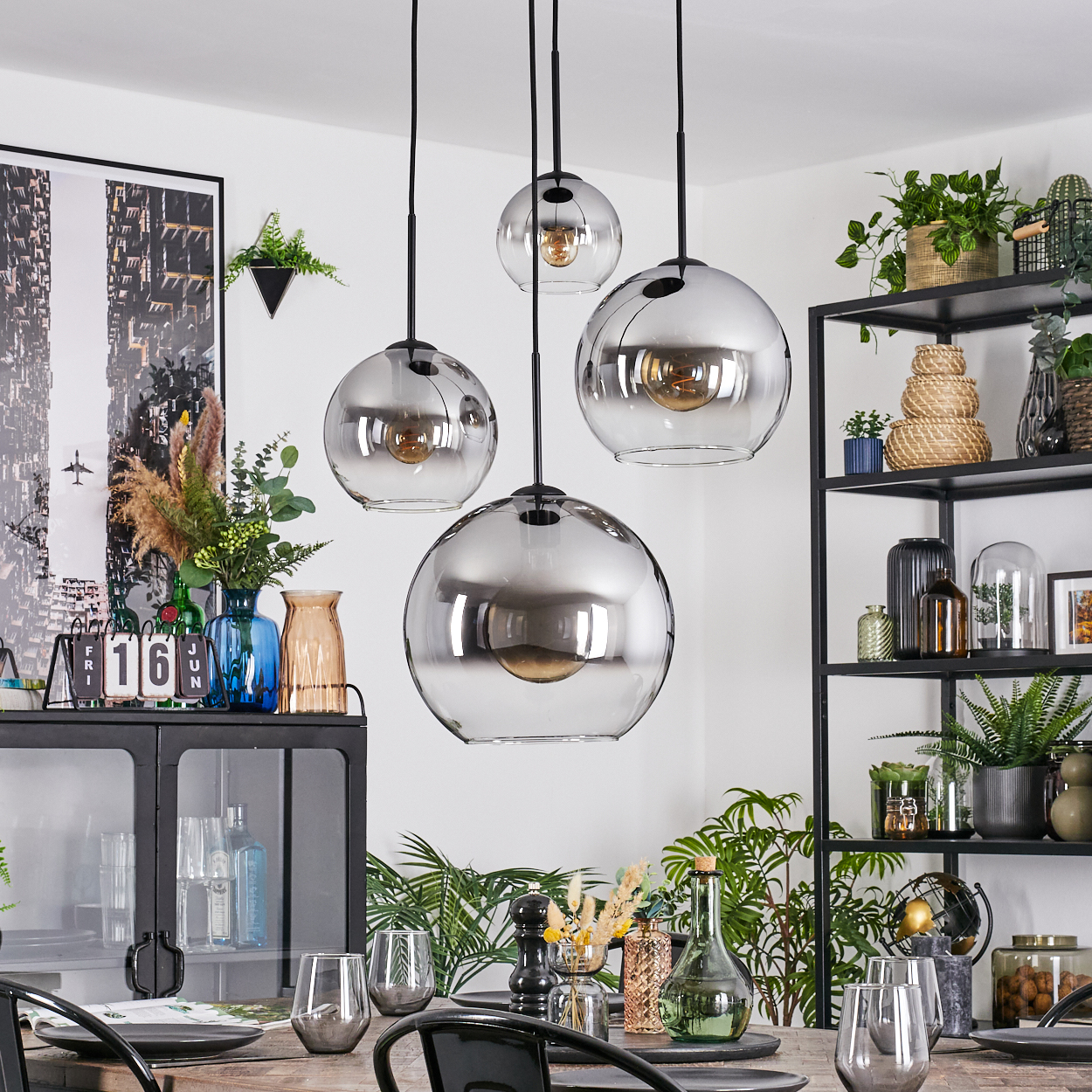 Esszimmer mit hängenden Kugelleuchten, Tisch mit Gläsern und ein schwarzes Regal mit Pflanzen und Dekorationen.