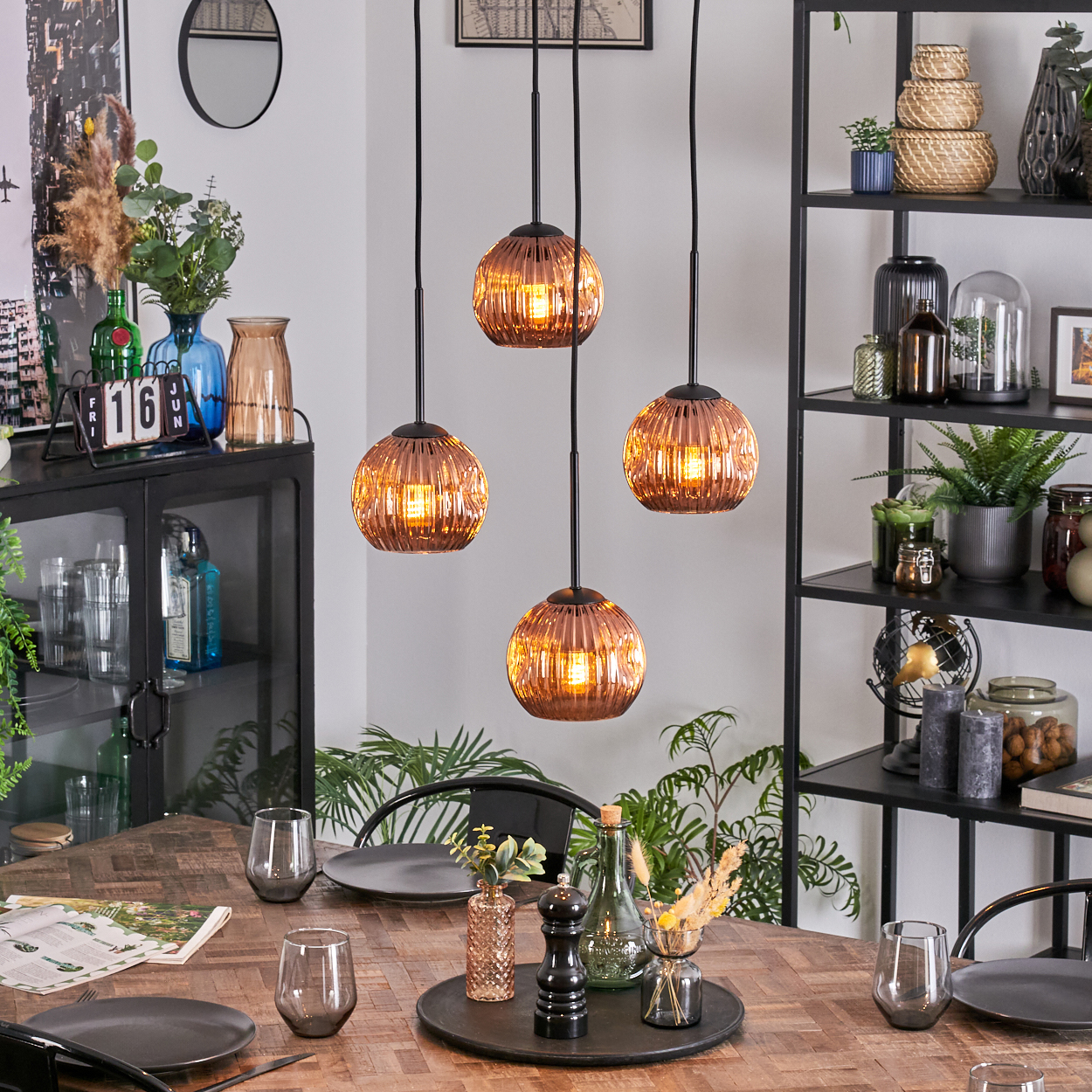 Esszimmer mit Holztisch, Hängelampen und Dekorationsartikeln. Pflanzen und Glaswaren sind ebenfalls zu sehen.