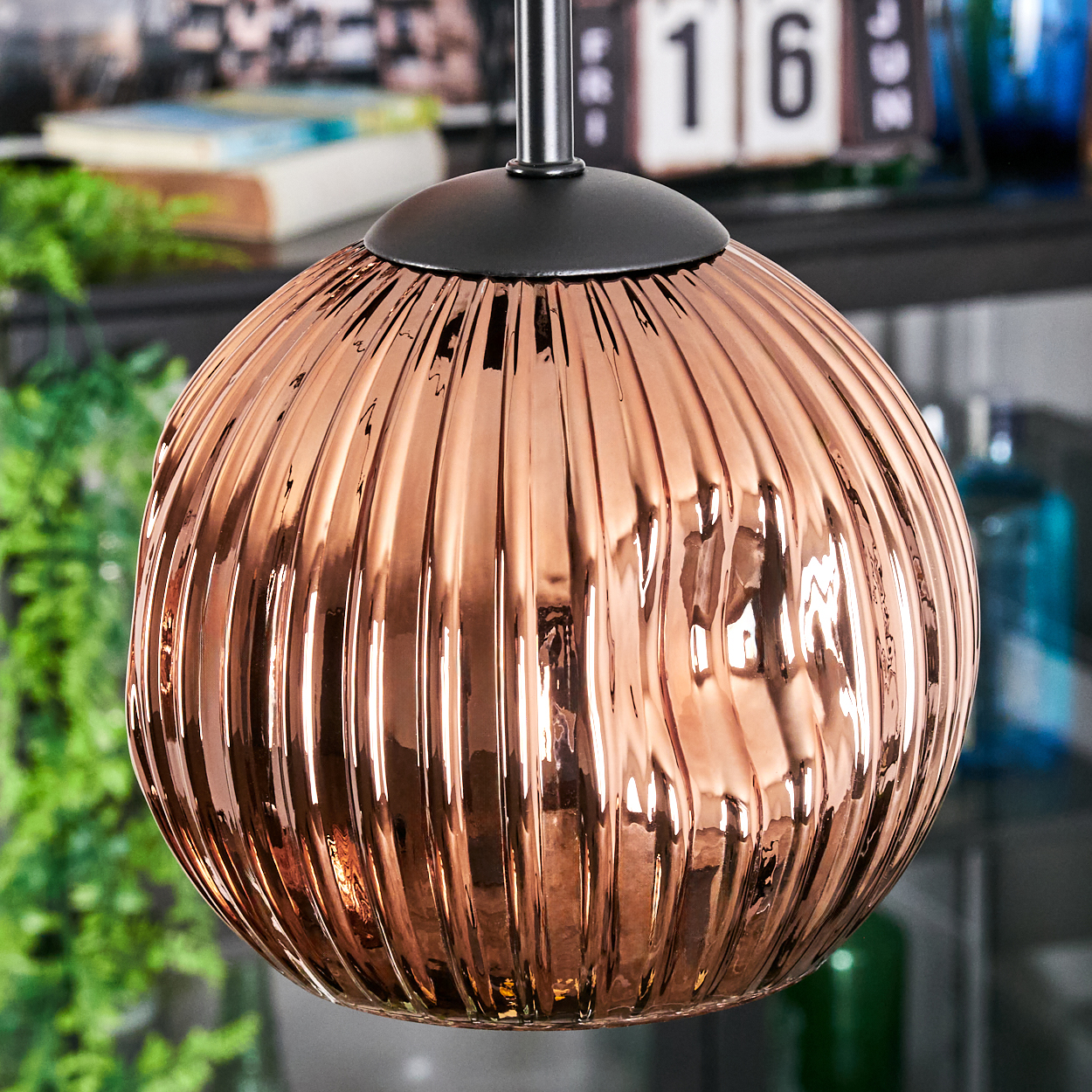 Eine kupferfarbene, gerippte Glas-Pendelleuchte hängt. Der Hintergrund hat einen Kalender mit der Zahl 16.