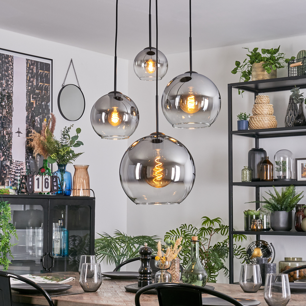 Esszimmer mit Hängekugelleuchten, gedecktem Tisch, Pflanzen und einem schwarzen Regal. Modernes und stilvolles Interieur.