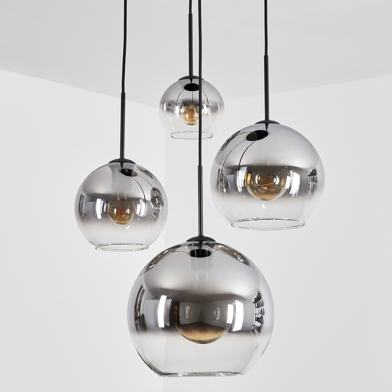 Vier kugelförmige, silber verspiegelte Pendelleuchten mit sichtbaren Glühbirnen hängen vor einer weißen Wand und Decke.