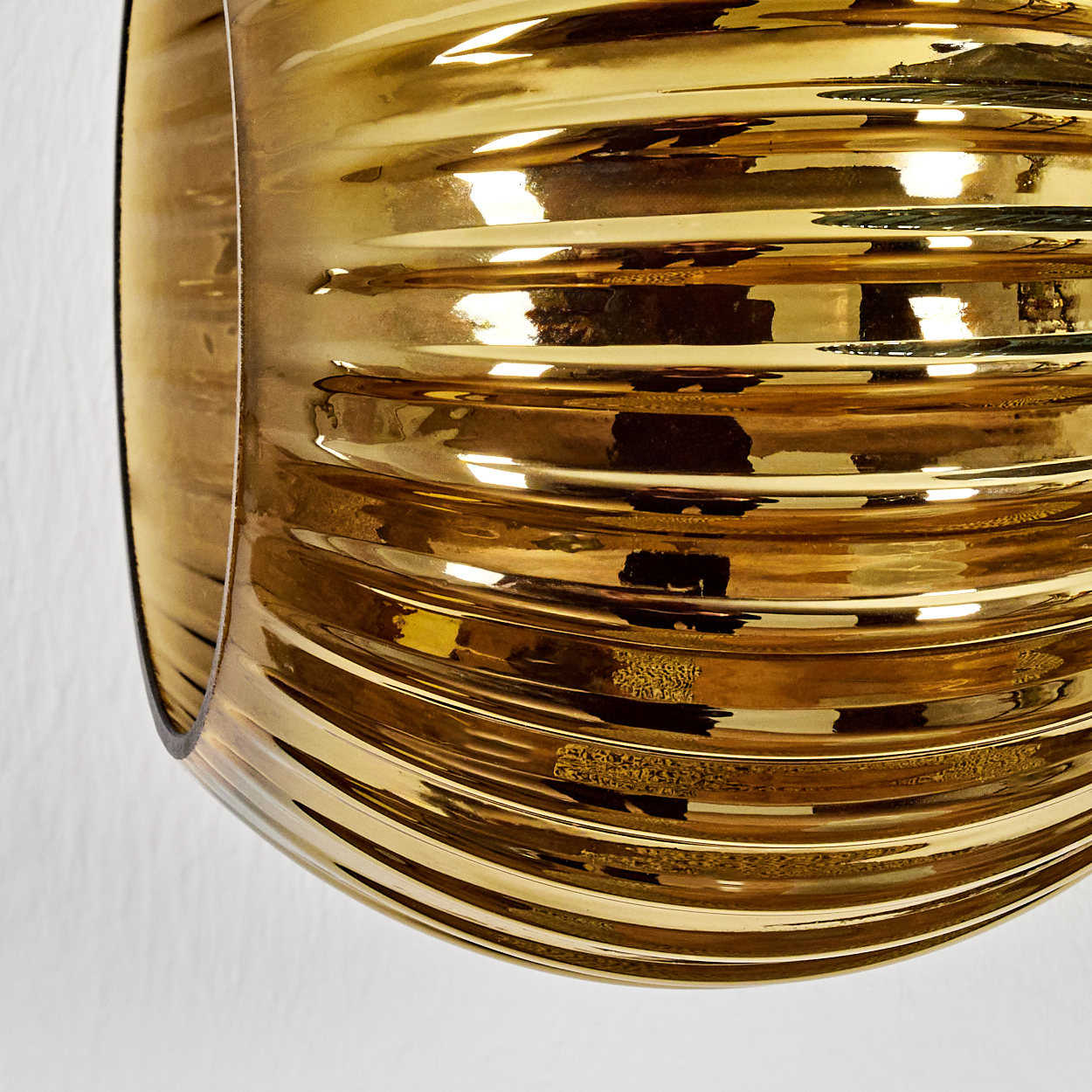 Nahaufnahme eines goldenen, gerippten, reflektierenden Objekts vor weißem Hintergrund. Das Objekt krümmt sich und zeigt Lichtreflexe.