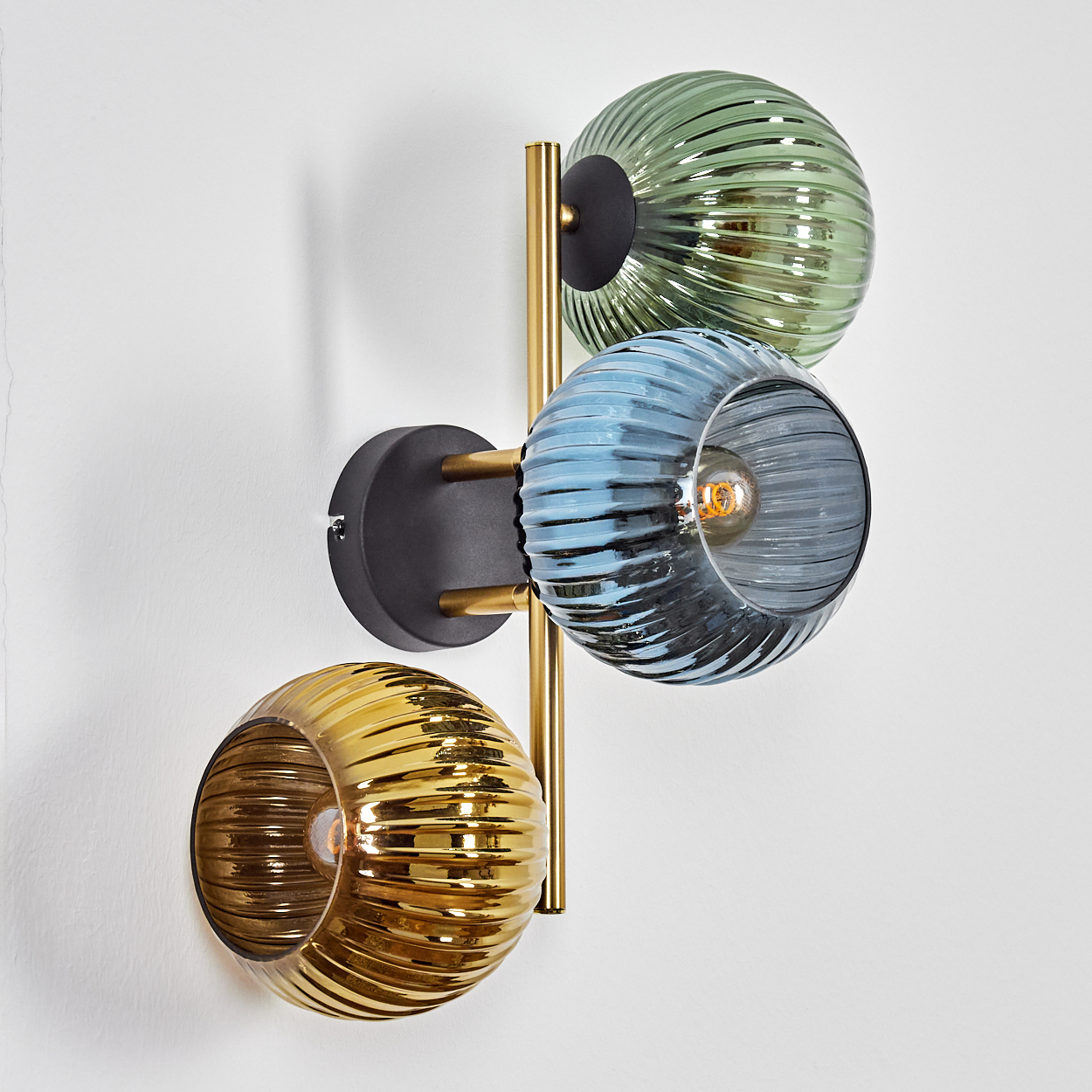 Wandleuchte mit drei Glaskugeln in Grün, Blau und Gold. Die Leuchte hat einen schwarzen Sockel und goldene Akzente.