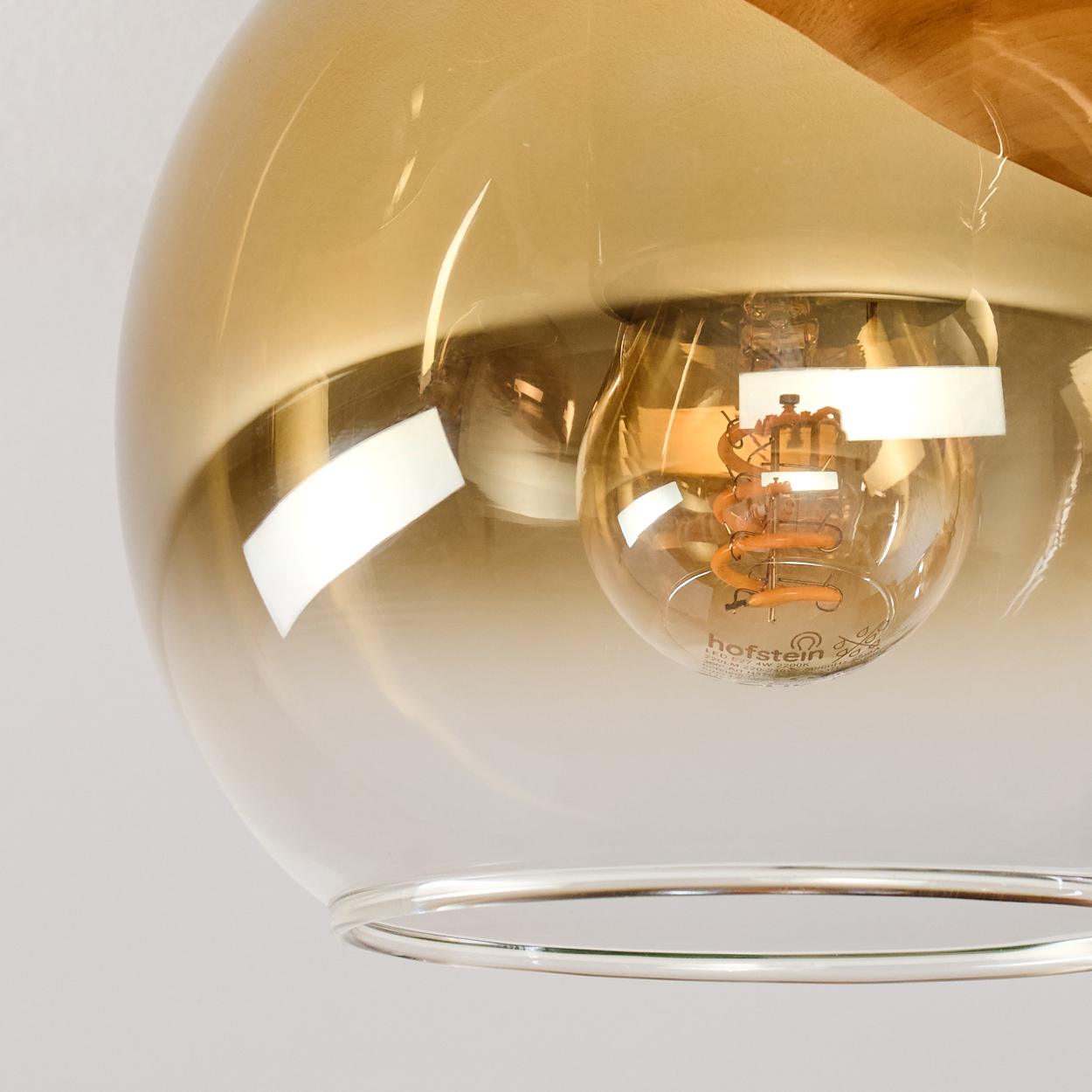 Nahaufnahme einer Glasleuchte mit einer Glühbirne. Das Glas ist bernsteinfarben und die Glühbirne leuchtet orange. Oben befindet sich ein Holzakzent.