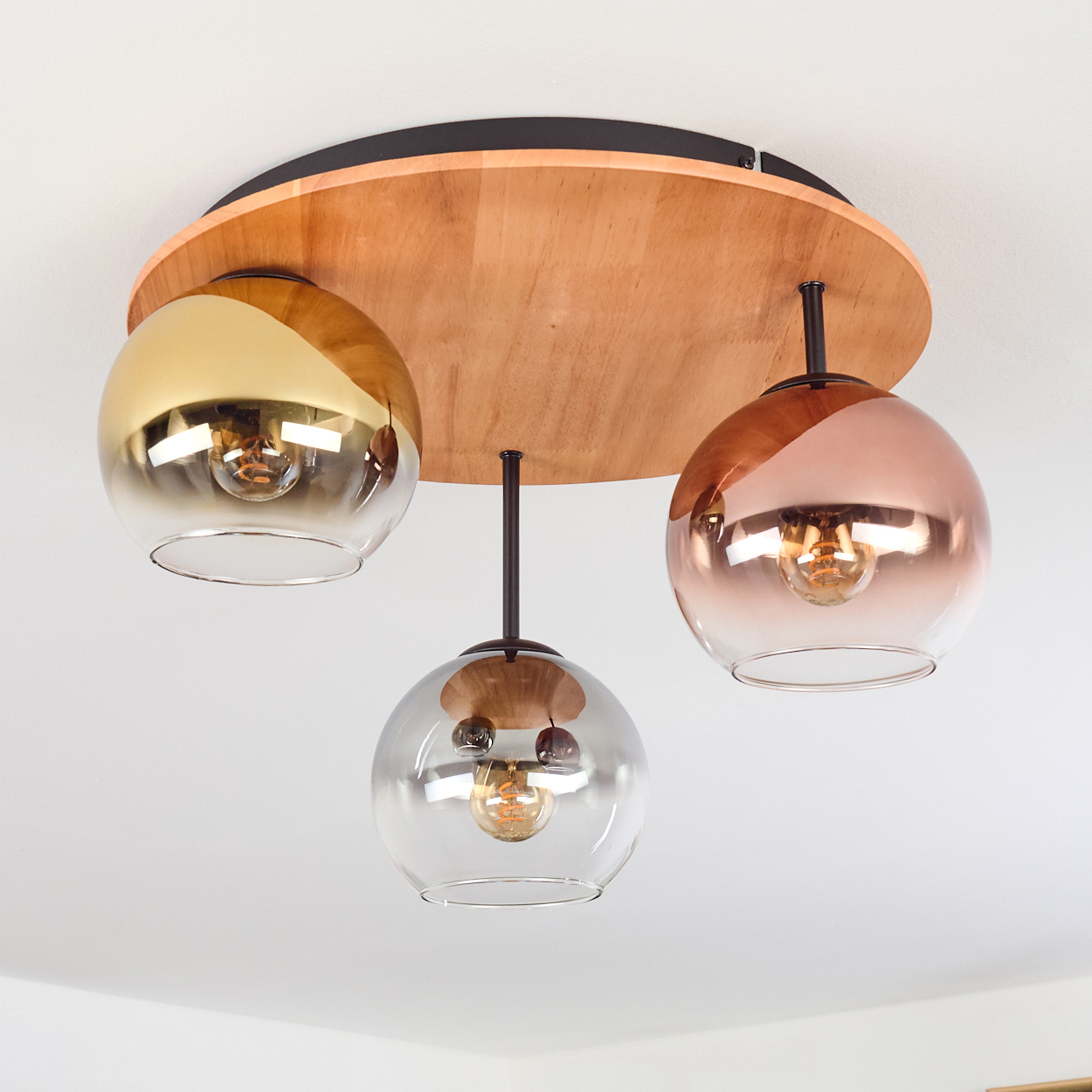 Eine moderne Deckenlampe mit drei Glaskugeln. Die Lampe hat einen Holzsockel und ist an einer weißen Decke befestigt.