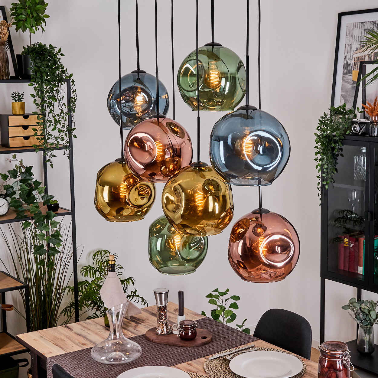 Esszimmer mit Holztisch, hängenden farbigen Kugellampen, Pflanzen und einem schwarzen Schrank.