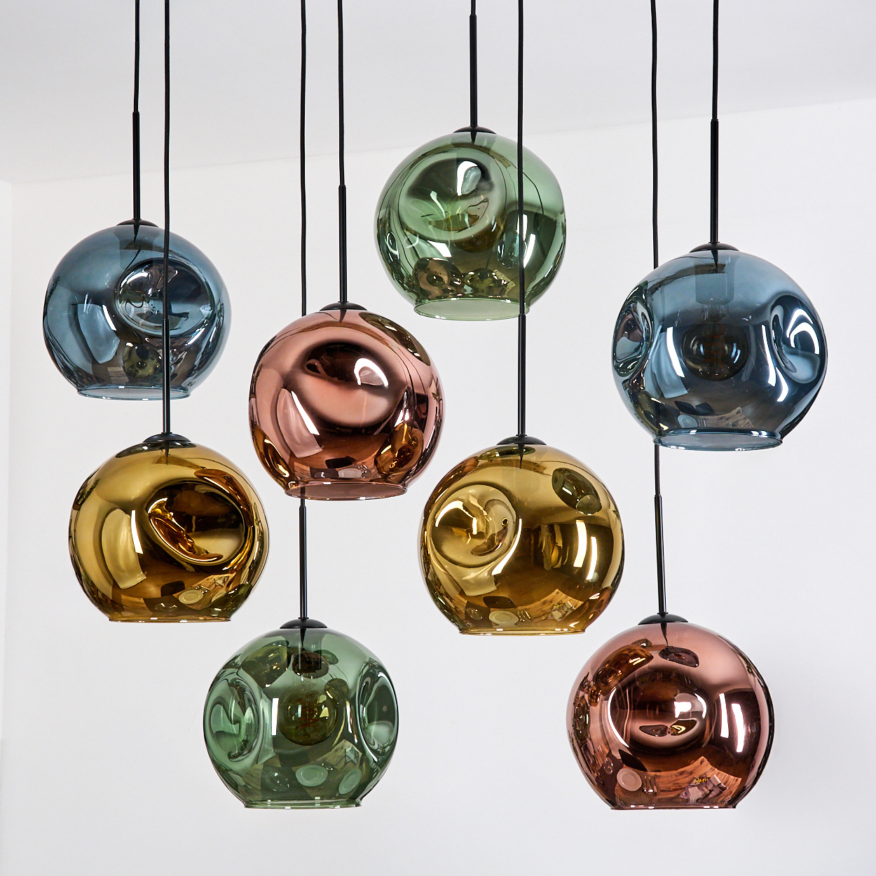 Acht kugelförmige Pendelleuchten. Farben sind Blau, Grün, Gold und Kupfer. Schwarze Kabel und Deckenhalterungen. Weißer Hintergrund.