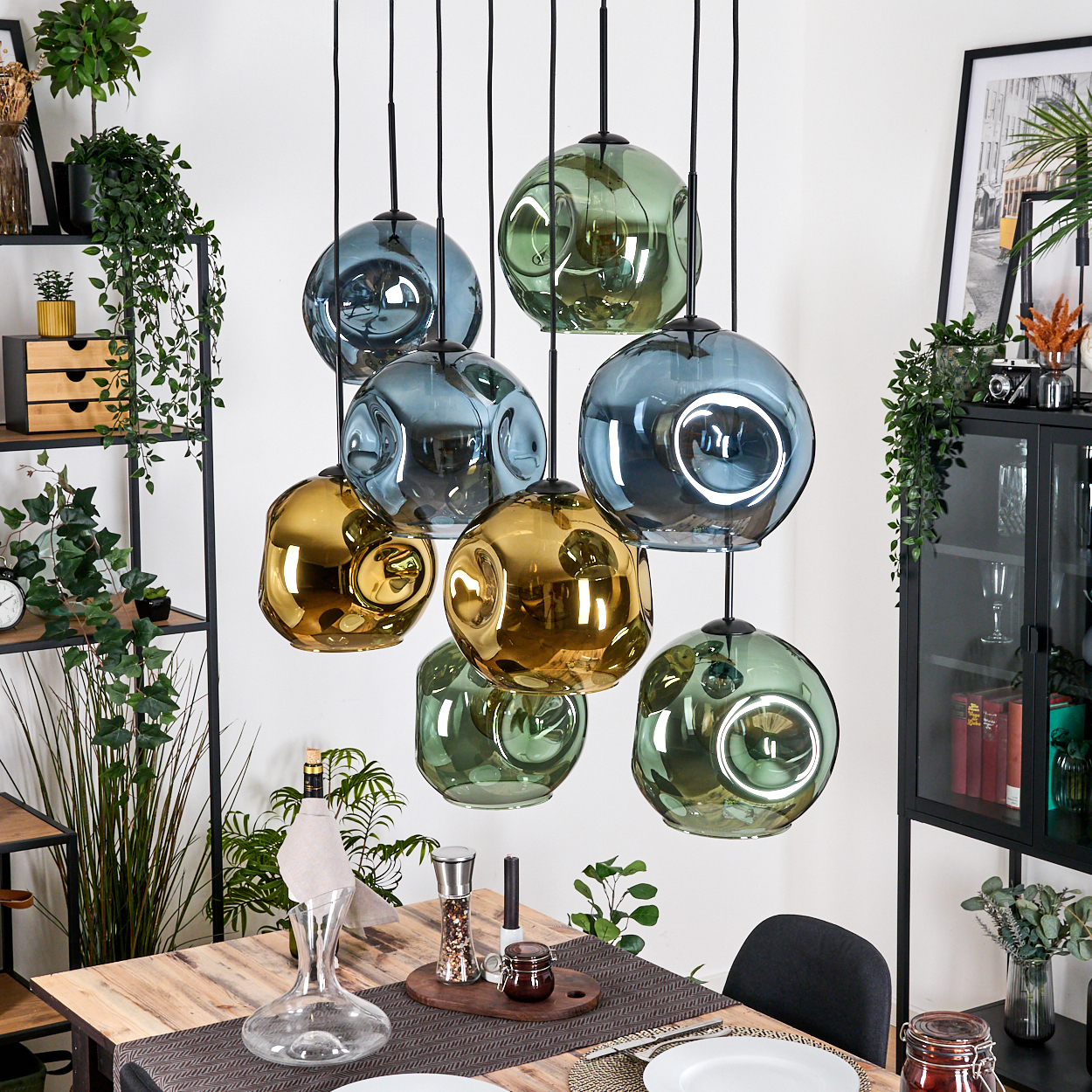 Esszimmer mit Holztisch, Glaskugelleuchten, Weindekanter und einem schwarzen Schrank mit Pflanzen.