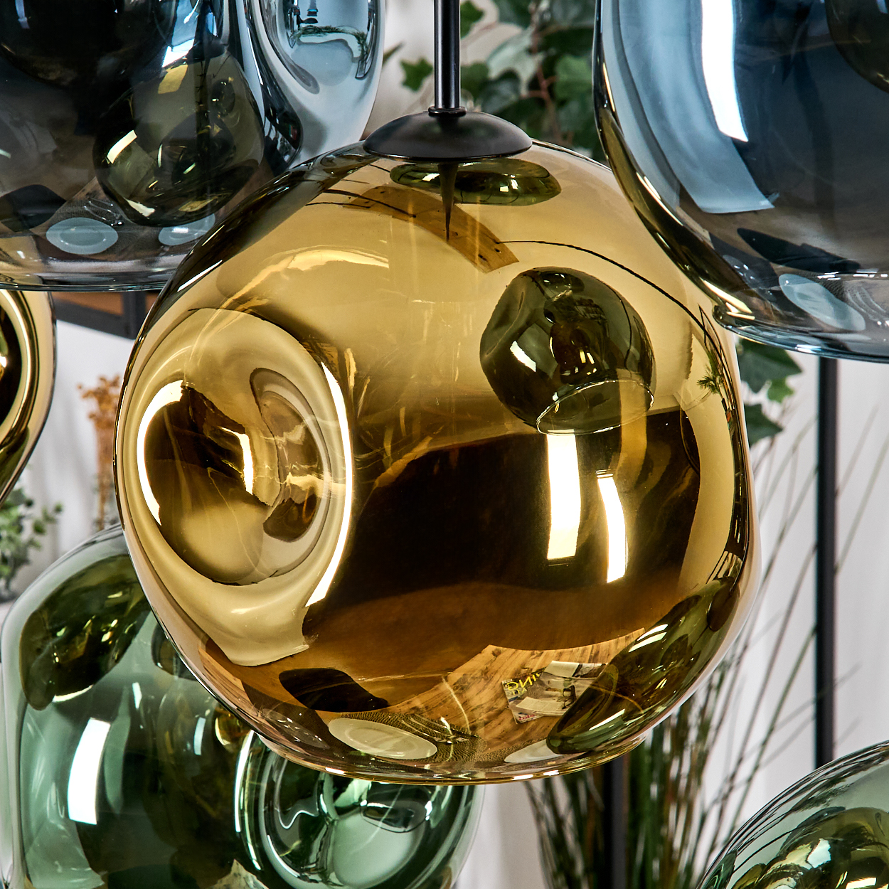 Nahaufnahme von Glas-Pendelleuchten. Das mittlere Licht ist goldfarben, umgeben von anderen in Grün- und Blautönen, alle reflektierend.