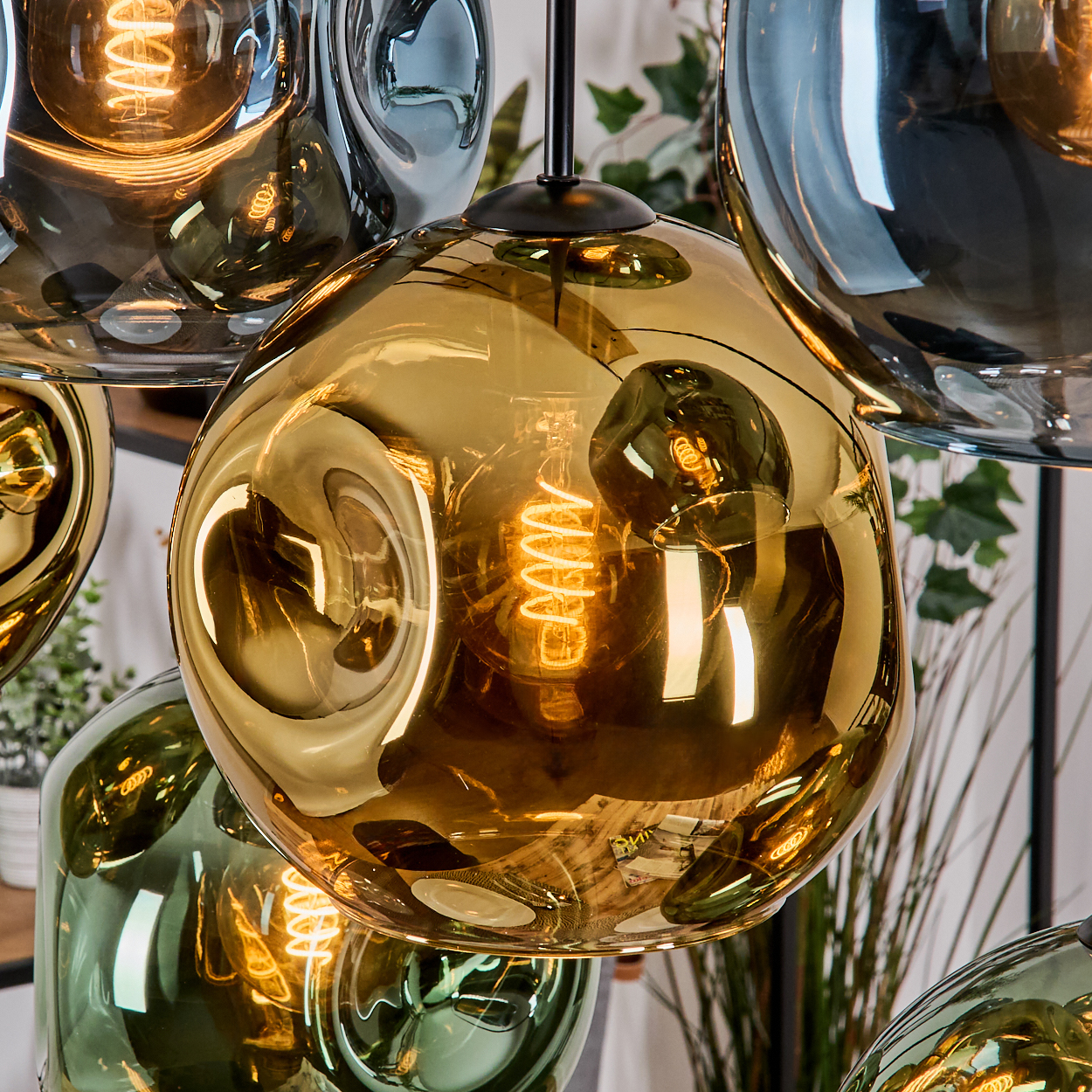 Nahaufnahme eines modernen Kronleuchters mit mehreren Glaskugeln in Gold, Grün und Grau. Jede Kugel hat eine sichtbare, warm getönte Glühbirne.